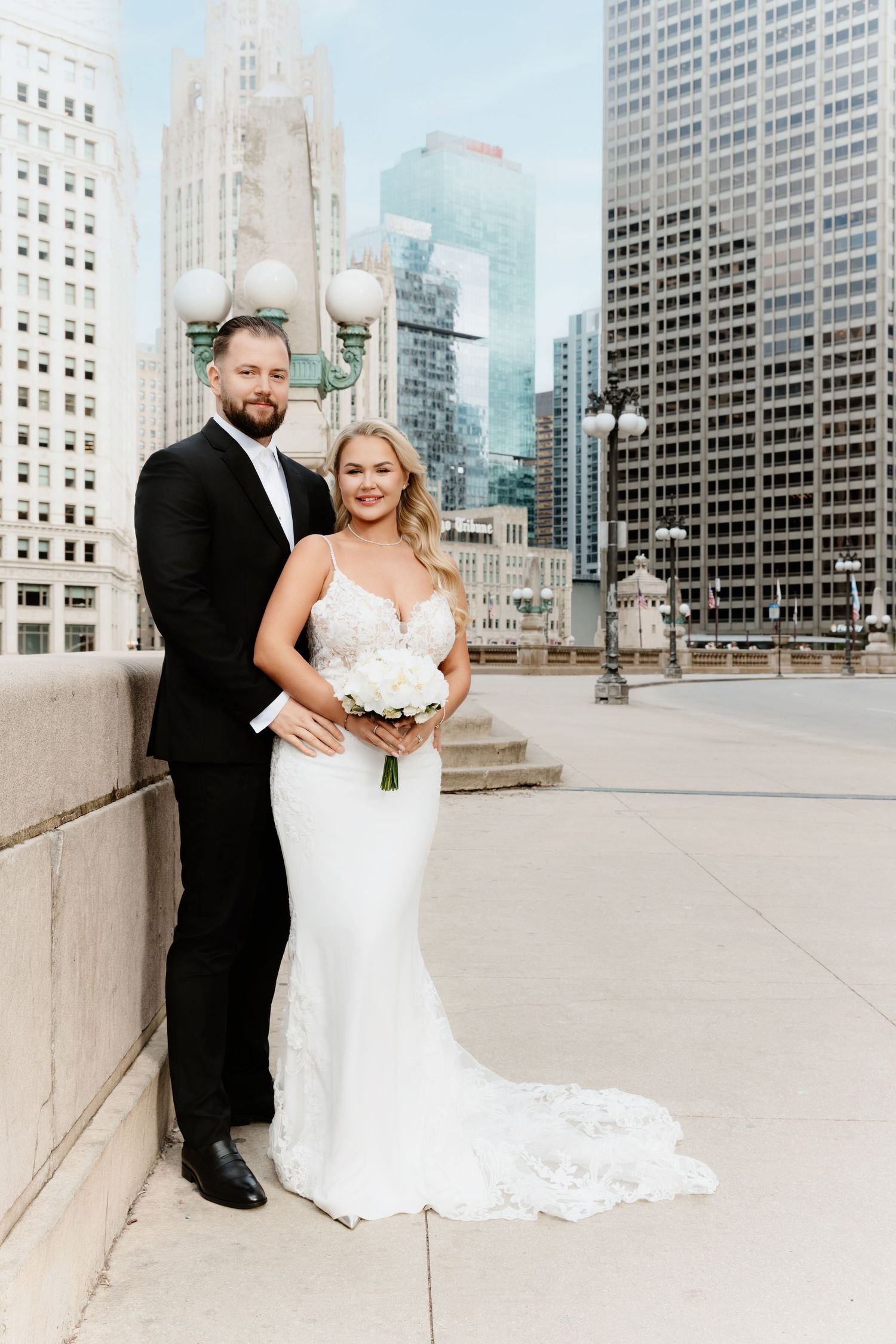 Smiling bride in mermaid gown and groom pose together on Chicago bridge with dramatic skyline backdrop.
