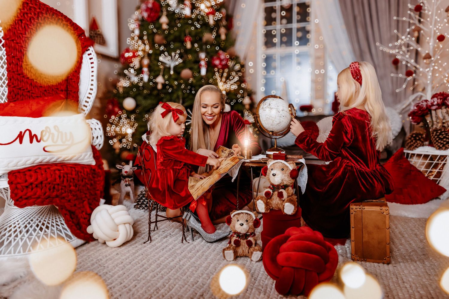 A mother and two children in red Christmas outfits share a magical moment near a decorated holiday tree.
