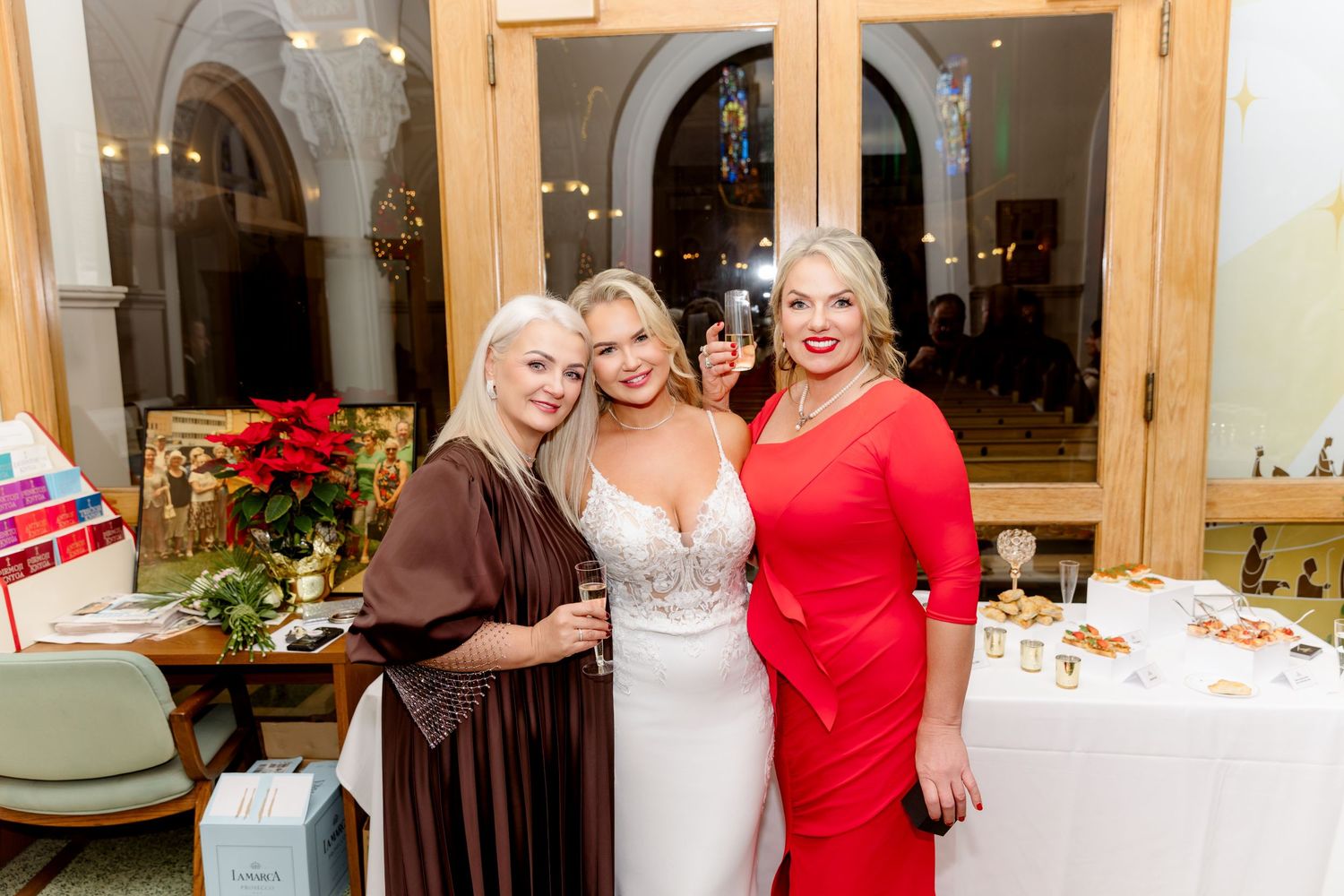 Three women posing at wedding reception, middle woman in white bridal gown.