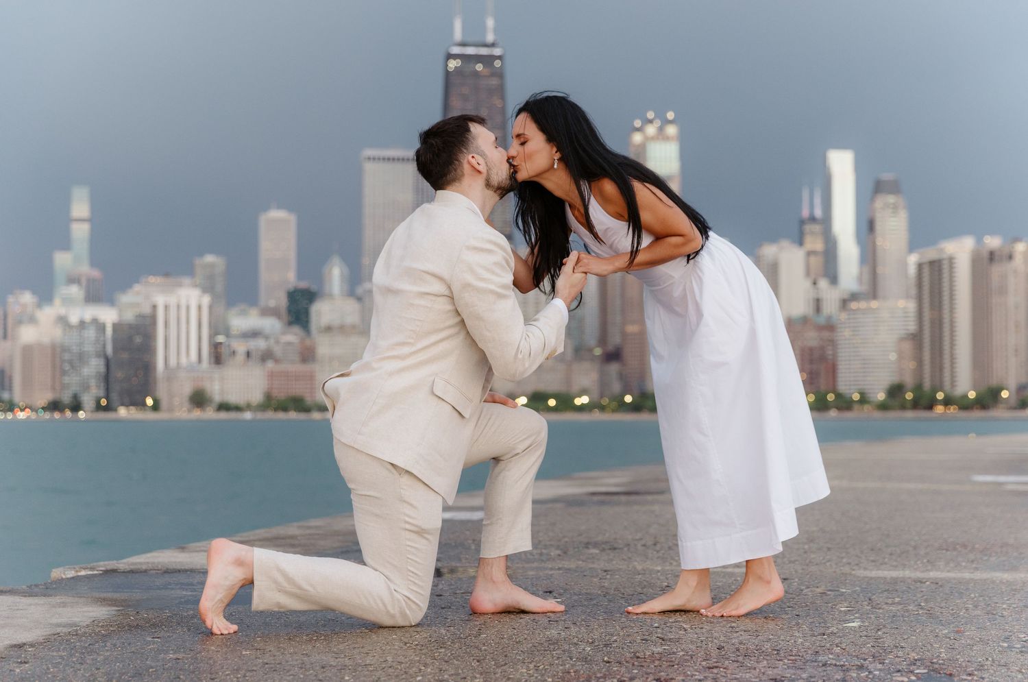 Couple sharing a kiss during marriage proposal on Chicago waterfront with skyline behind.