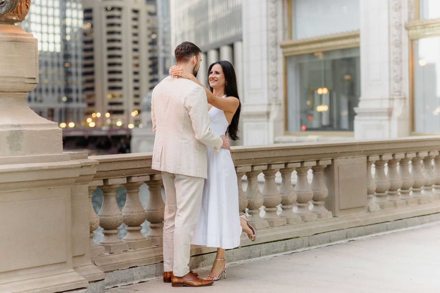 Elegant couple embracing on a stone balcony with Chicago skyscrapers in the background.