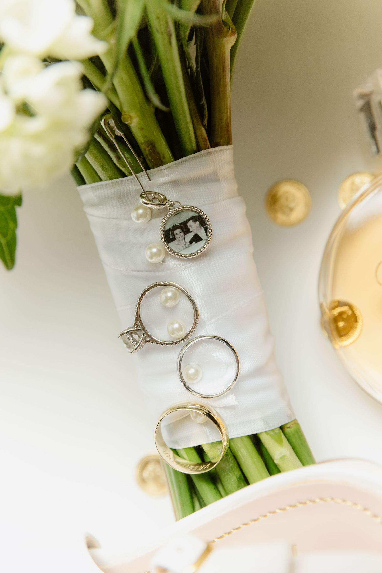 Wedding rings and diamond engagement ring displayed on bouquet stems with pearl charm necklace.