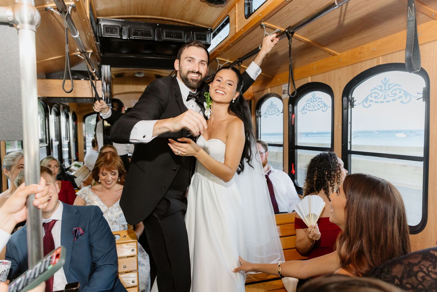 Bride and groom dancing joyfully on vintage trolley with wedding guests.