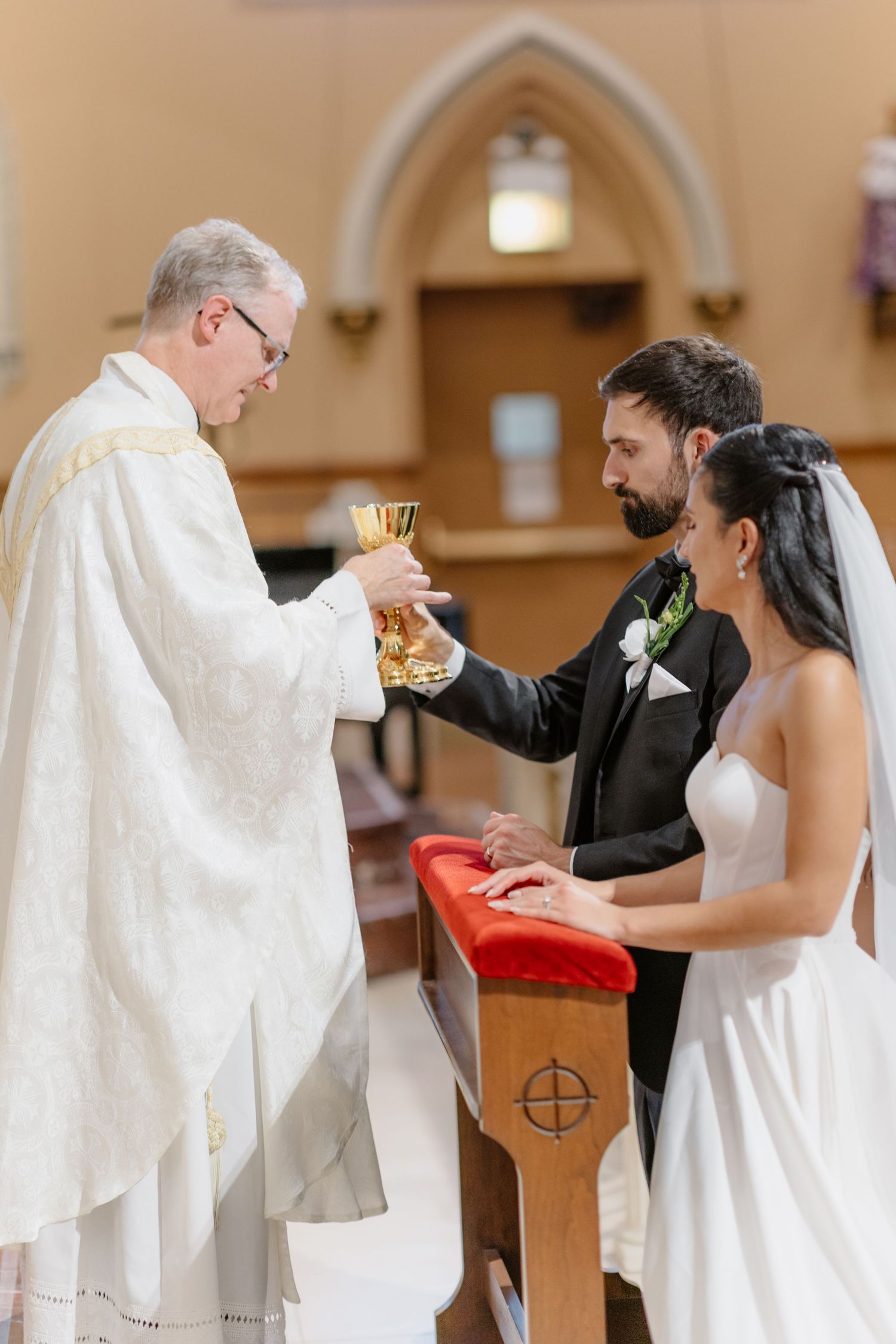 Priest offering communion chalice to bride and groom during Catholic wedding ceremony at church altar.