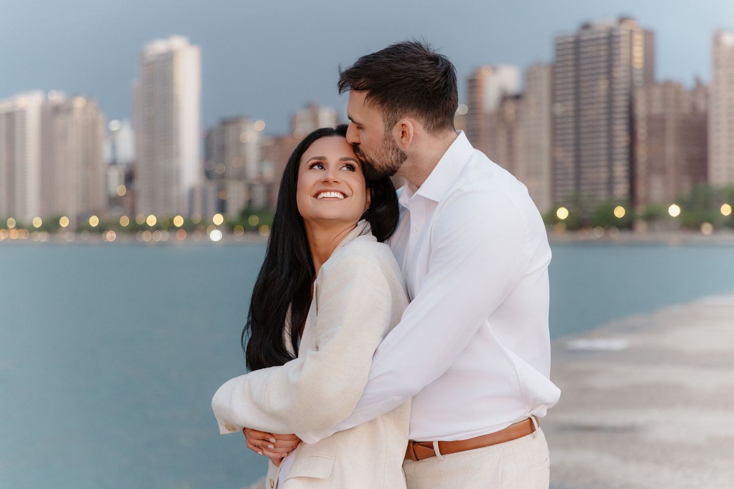 Romantic couple sharing tender moment by Lake Michigan with Chicago skyline during engagement session.