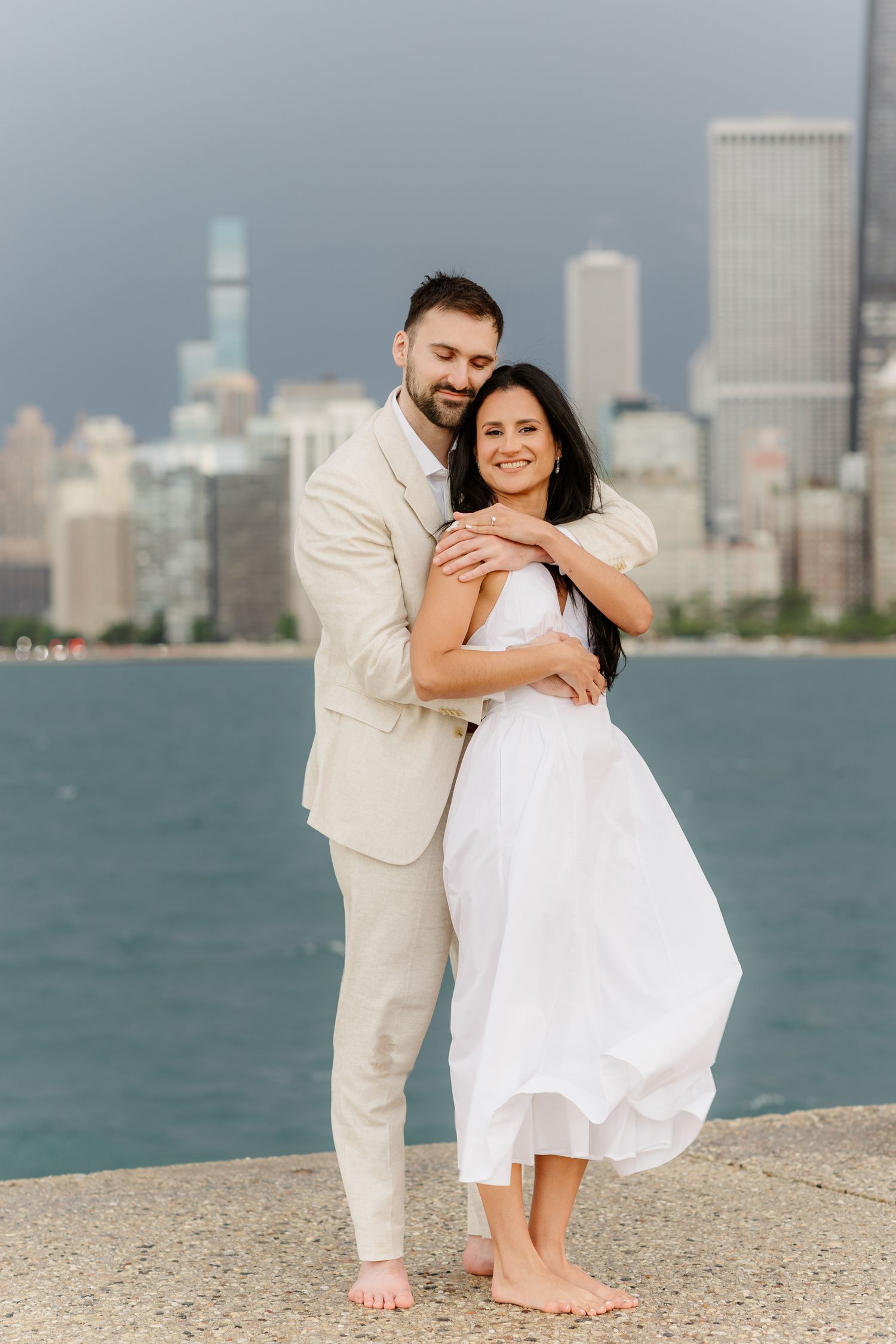 Happy couple embracing on Chicago waterfront, man in beige suit hugging woman in white dress.