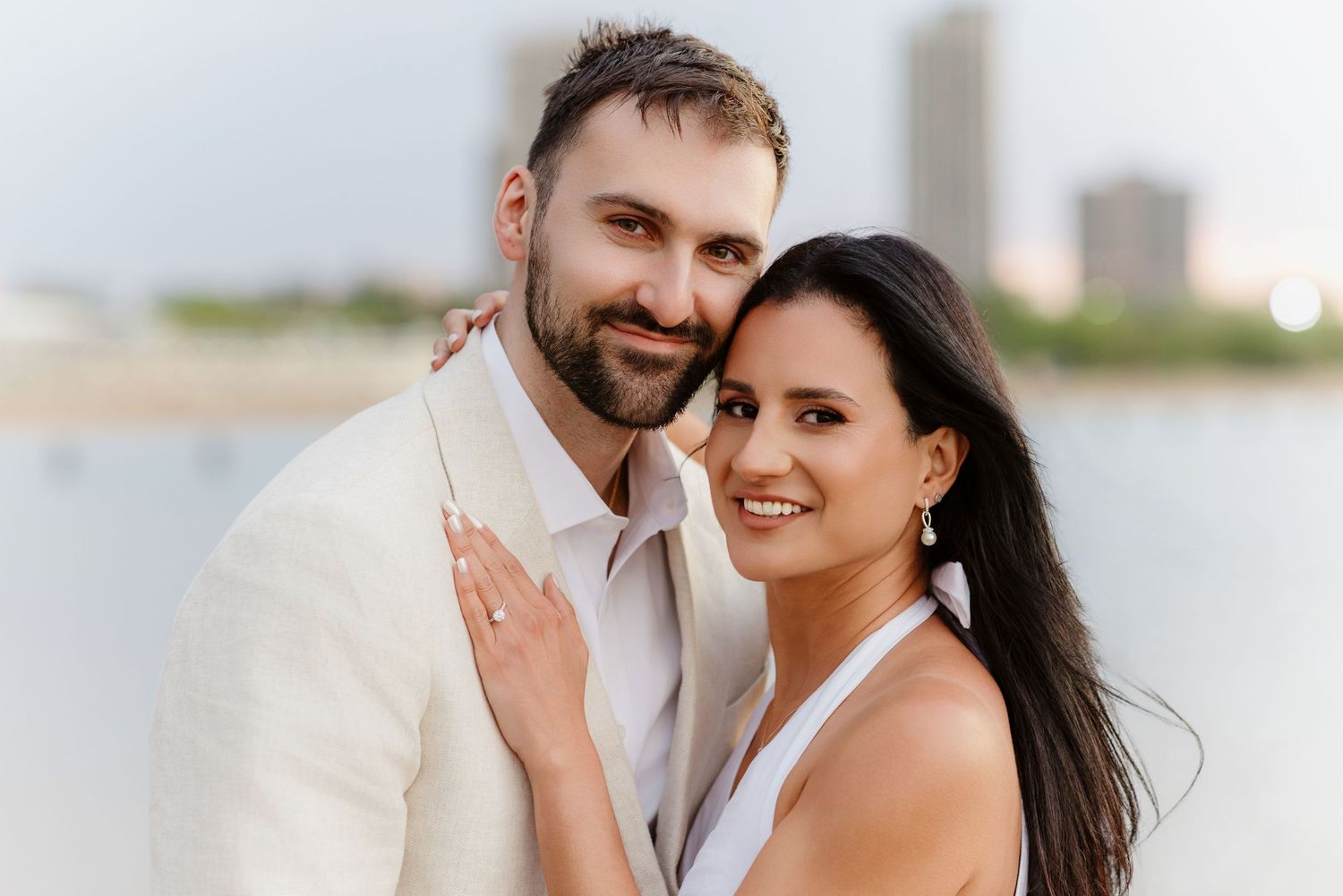 Happy smiling couple posing together for engagement portrait with lakeside city backdrop.
