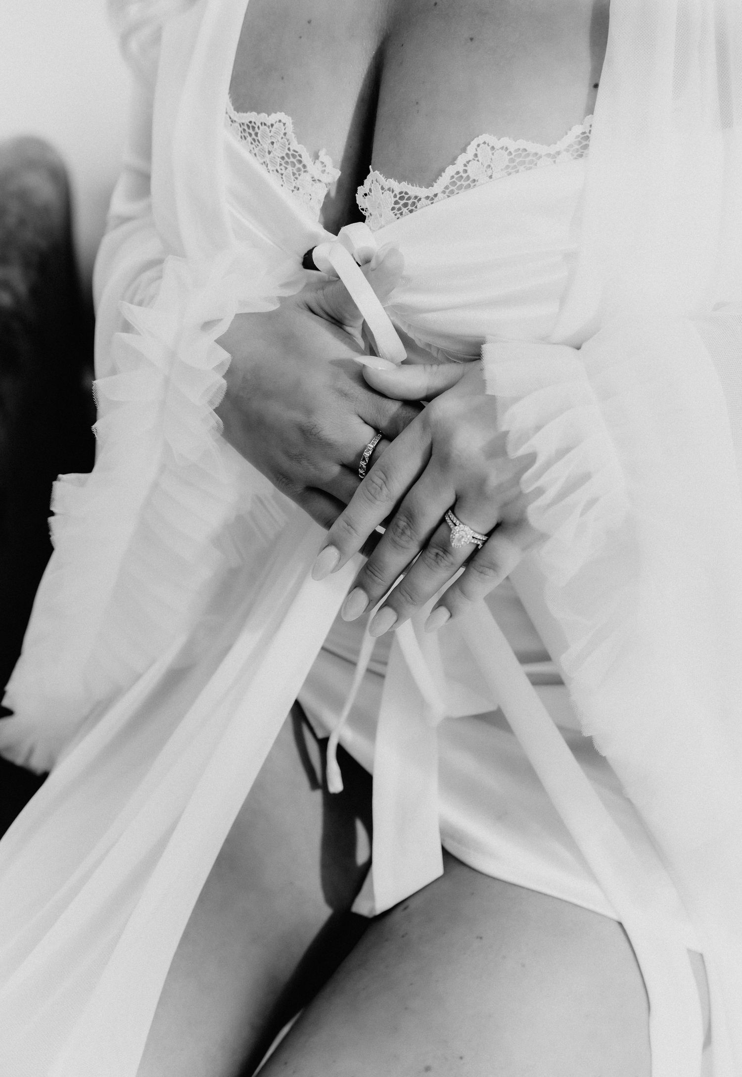 Black and white close-up of bride's hands with rings in white lace bridal lingerie.