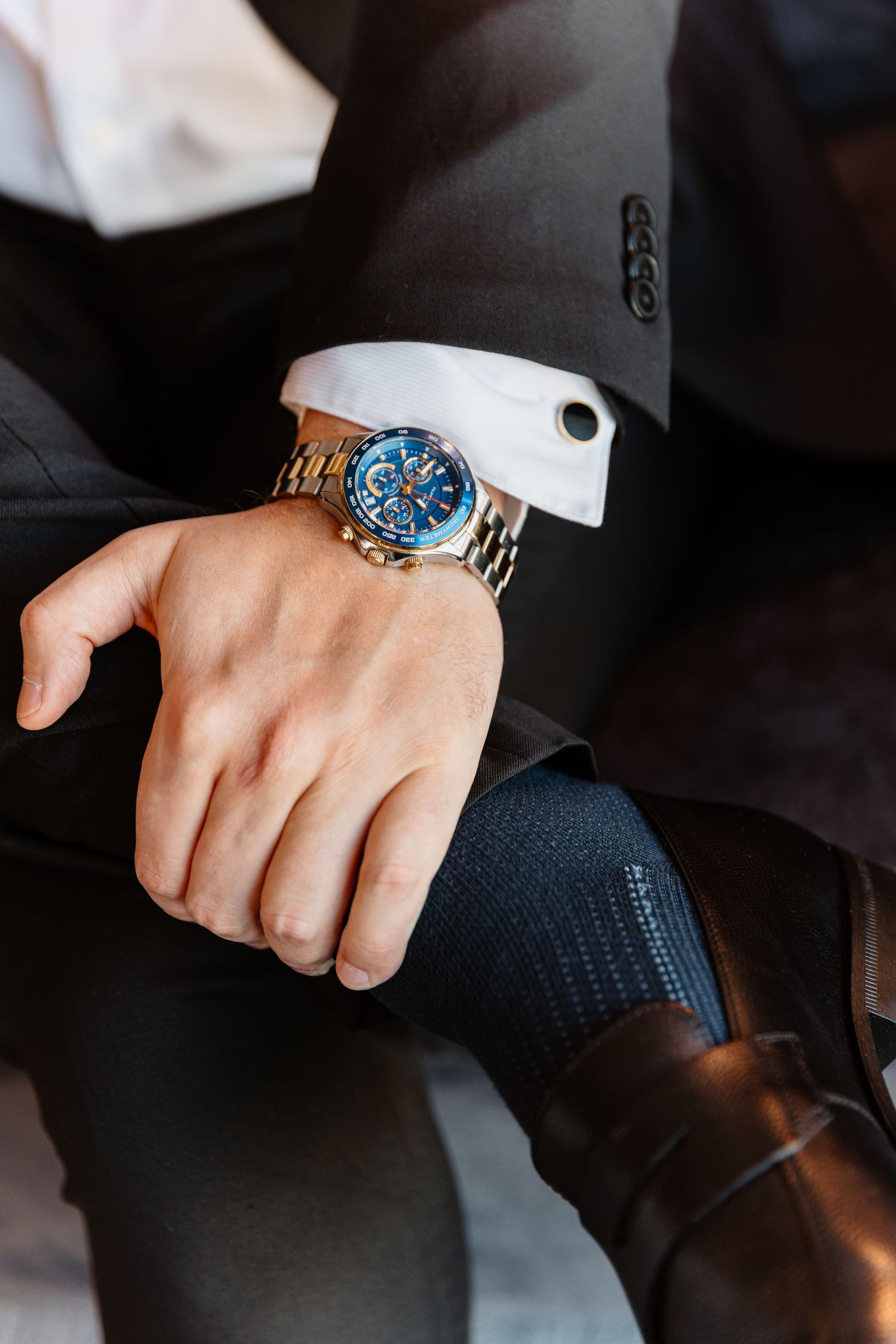 Close-up of groom's wrist wearing luxury blue dial gold chronograph watch with suit cufflink.