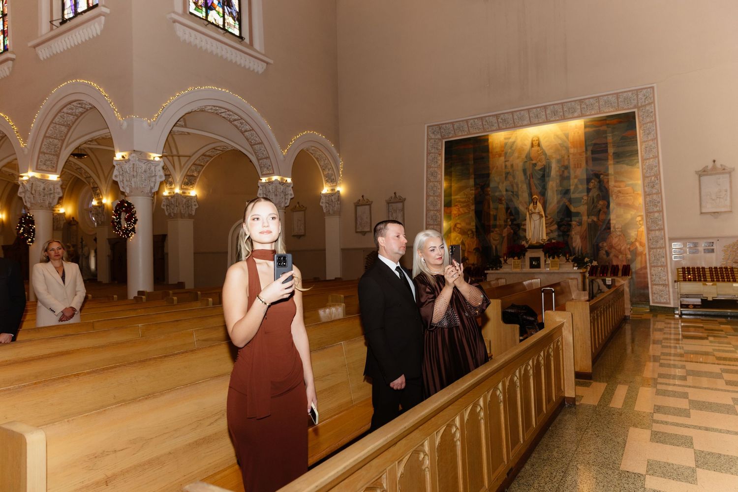 Wedding singer in burgundy dress performs while guests stand in beautifully decorated church aisle.