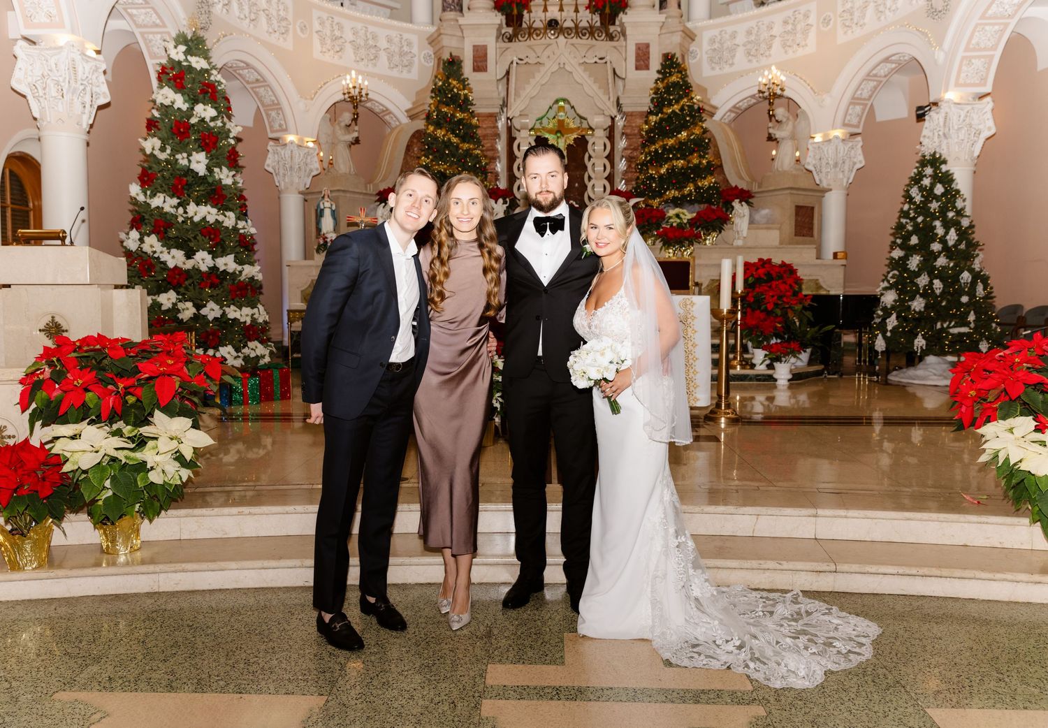 Bride groom and two guests posing together in elegant Christmas-decorated church with poinsettias.