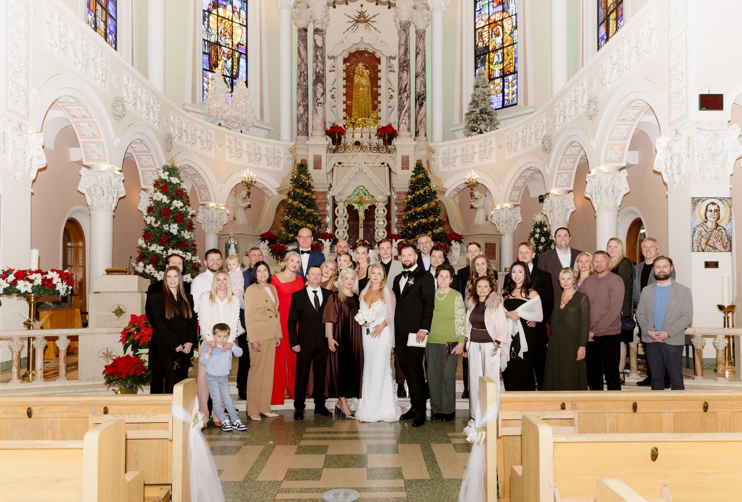 Large wedding group portrait inside elegant white Catholic church decorated with Christmas trees and holiday decor.