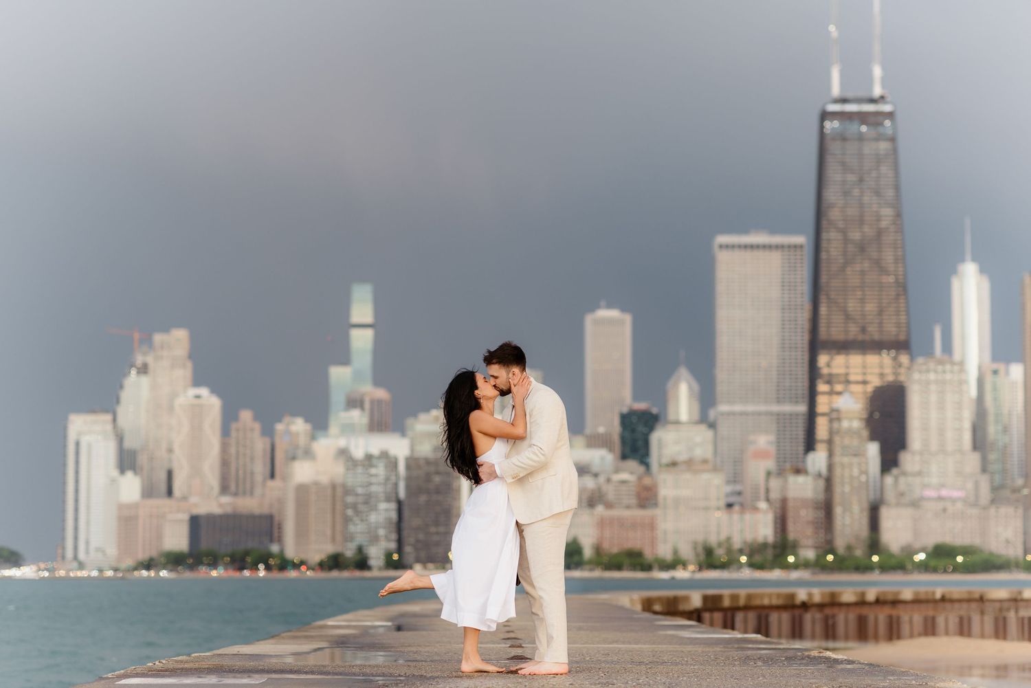 Couple shares romantic kiss on Chicago lakefront pier with John Hancock Center visible in background.