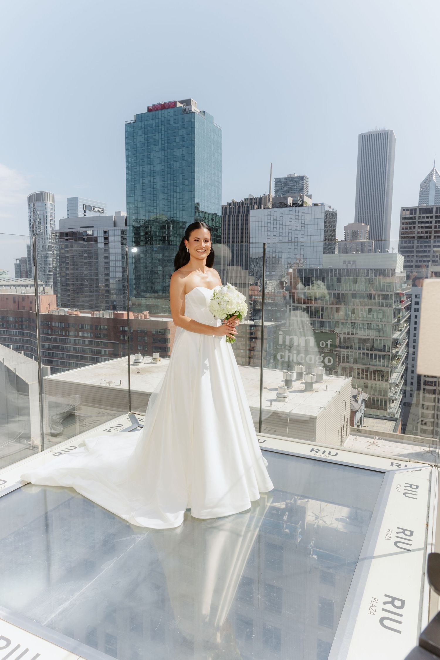Elegant bride in flowing white ball gown posing on rooftop with Chicago city skyline.
