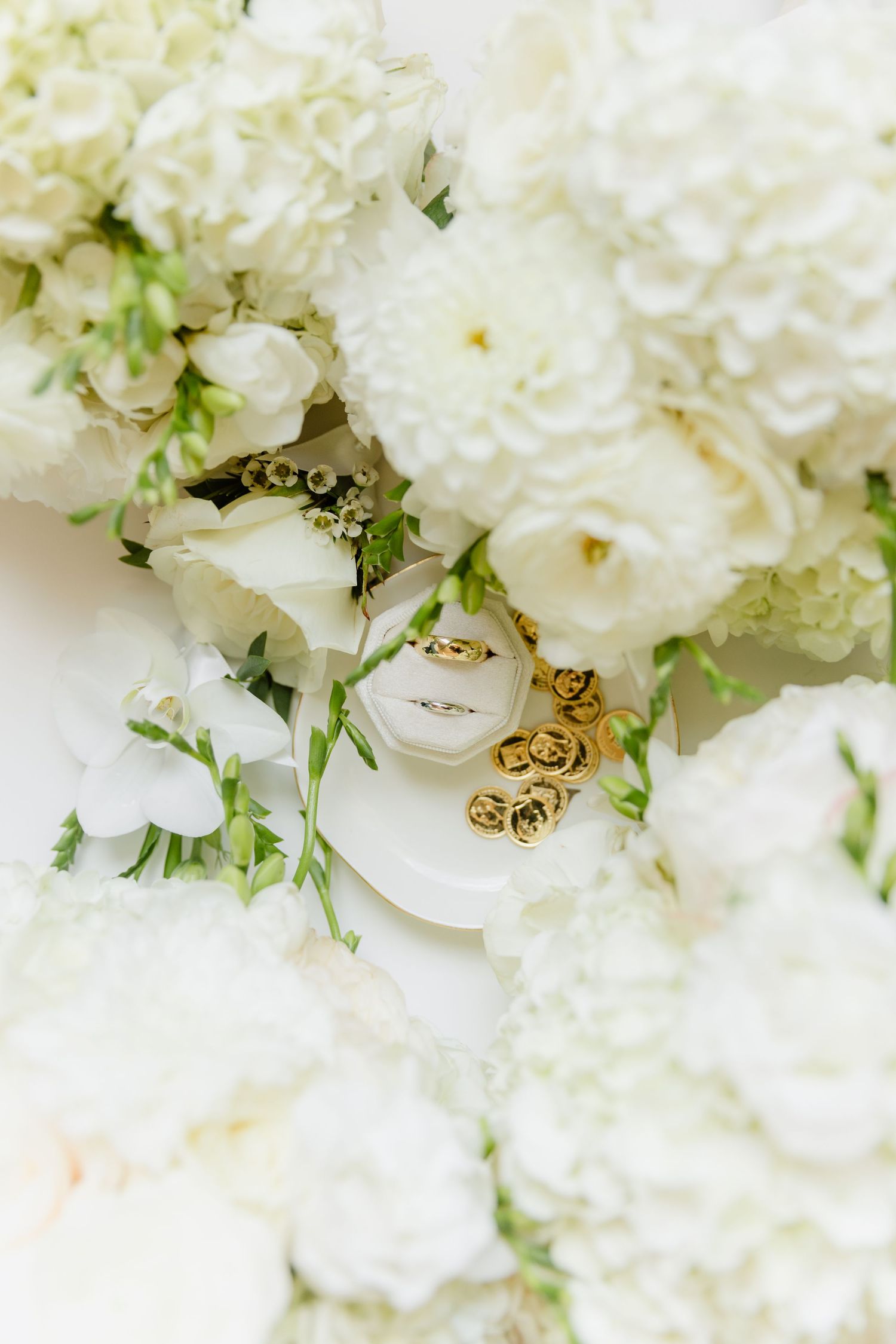 White wedding bouquets surround a ring box with gold earrings and diamond engagement ring.