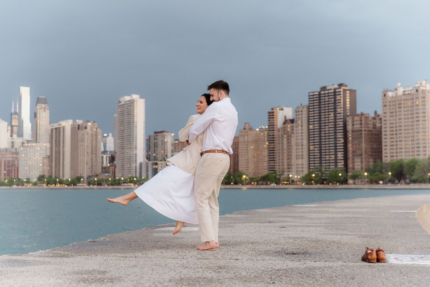 Couple dancing barefoot on Chicago lakefront pier with stunning city skyline in background.