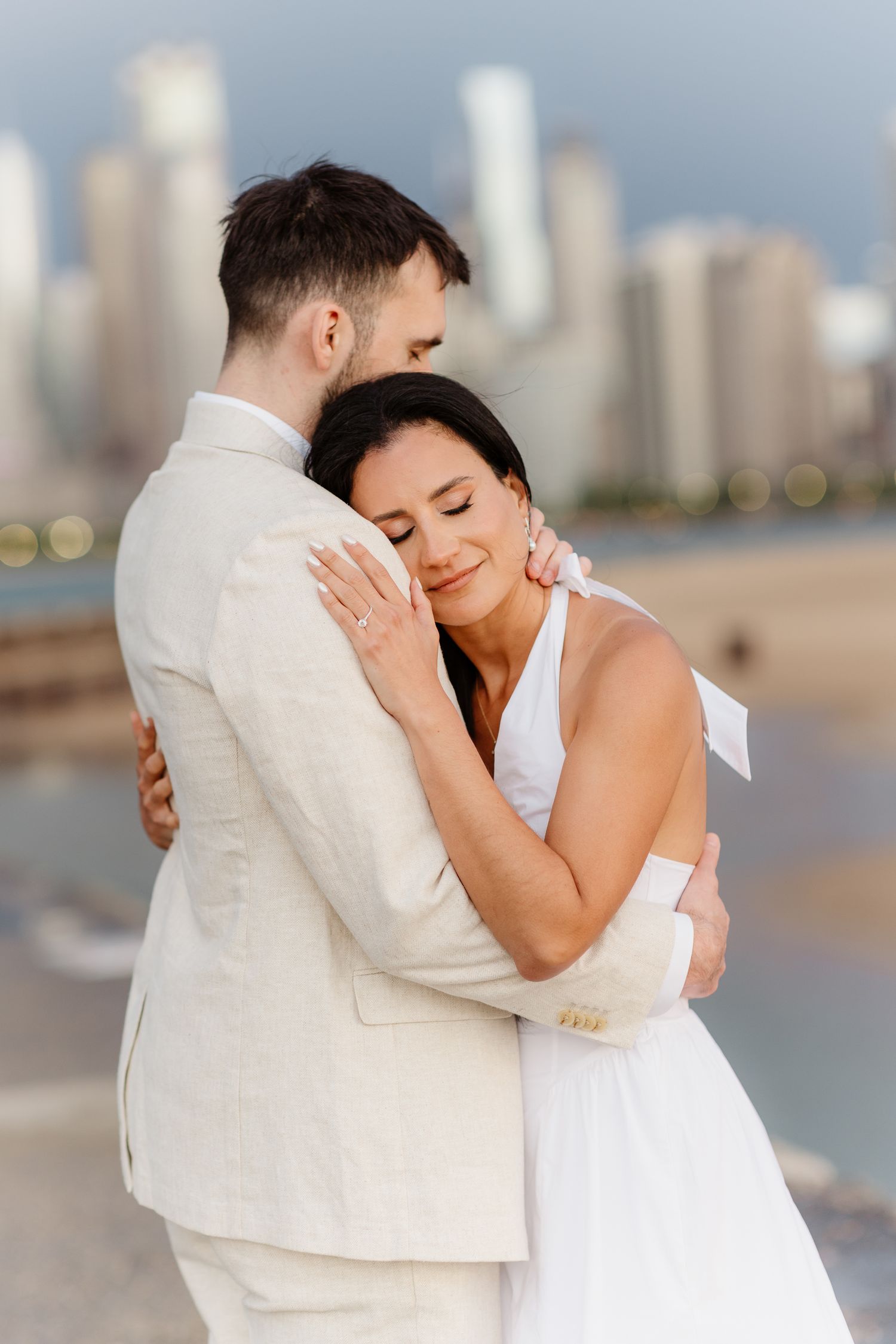 Bride with closed eyes resting head on groom's chest while embracing near Chicago waterfront at golden hour.