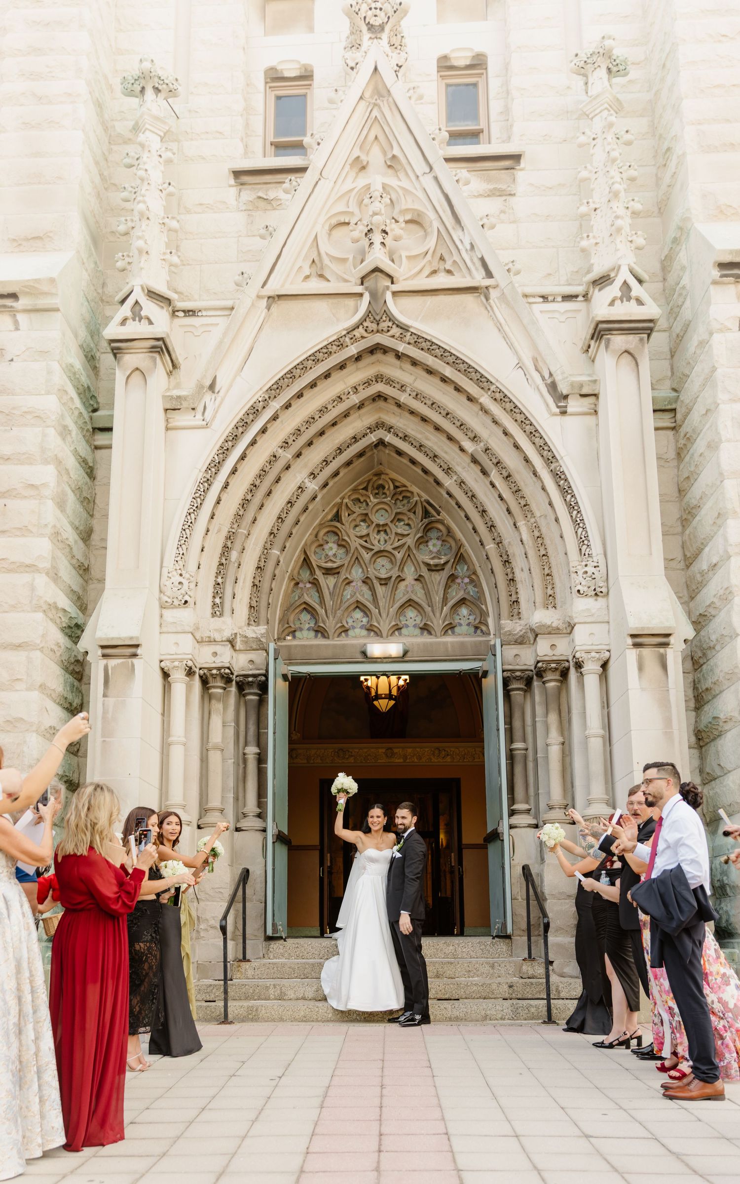 Bride and groom exit grand Gothic cathedral as guests cheer during wedding recessional.