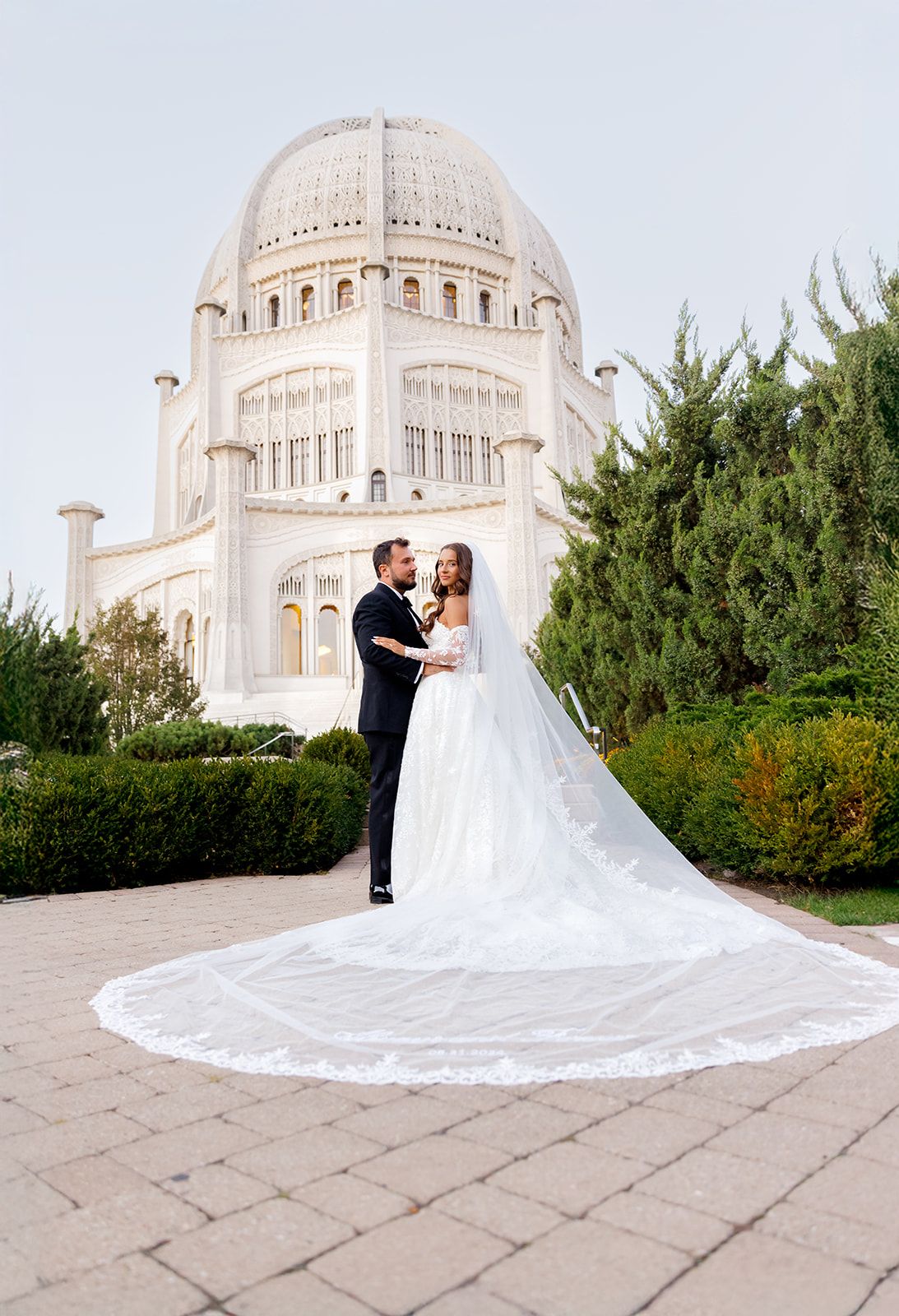 Bride and groom pose before the Bahá'í Temple in Wilmette, Illinois, with an elegant cathedral veil trailing on the pavement.