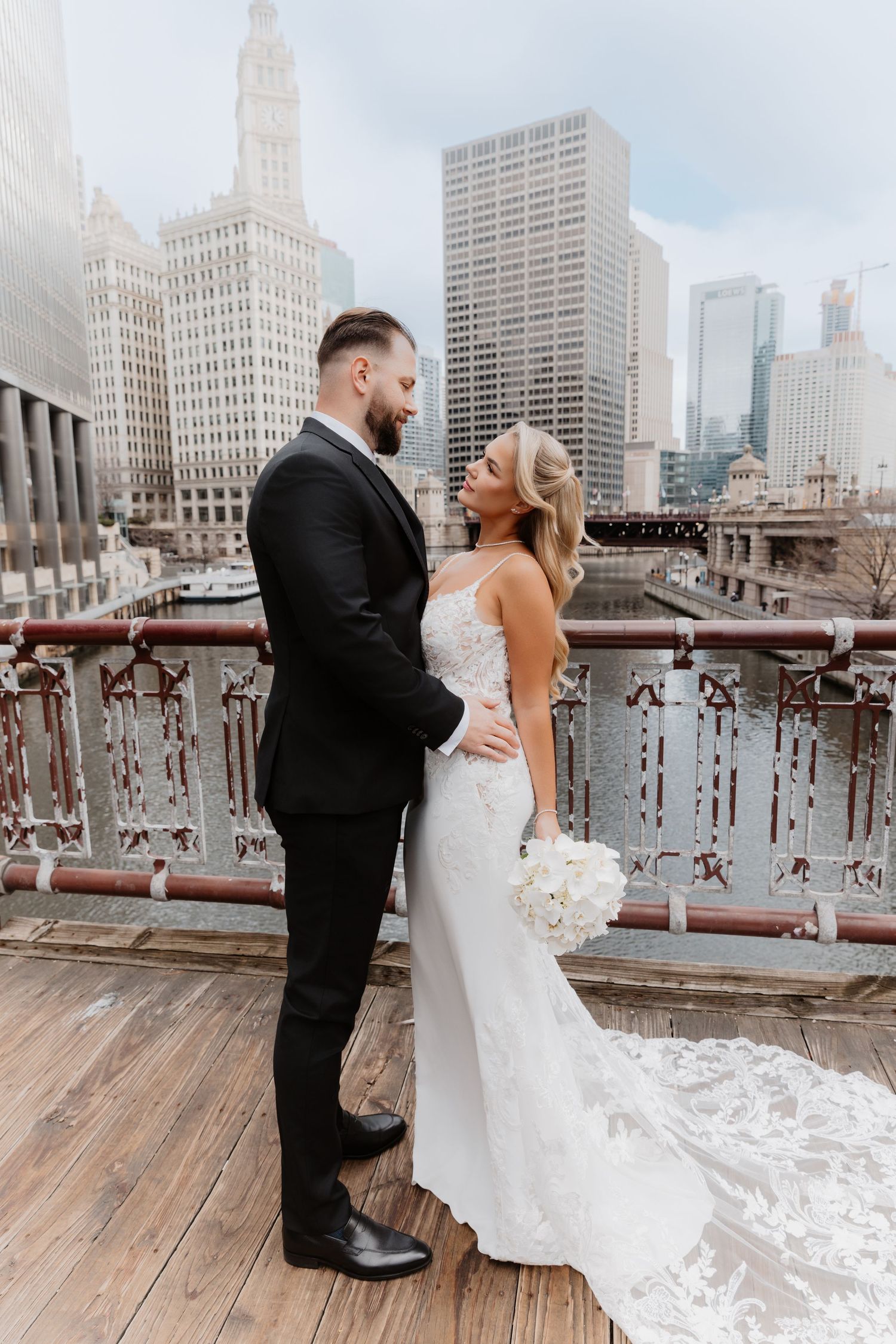 Bride and groom share romantic moment on Chicago bridge, bride in lace mermaid gown holding white bouquet.