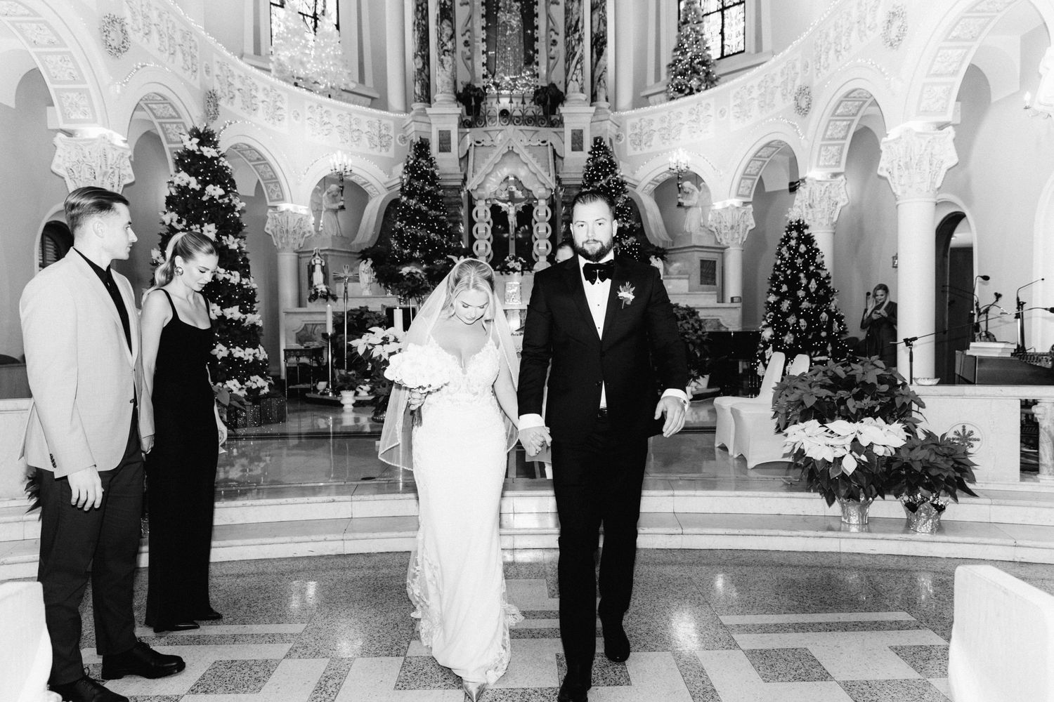 Black and white photo of newlyweds walking down church aisle after wedding ceremony with guests watching.