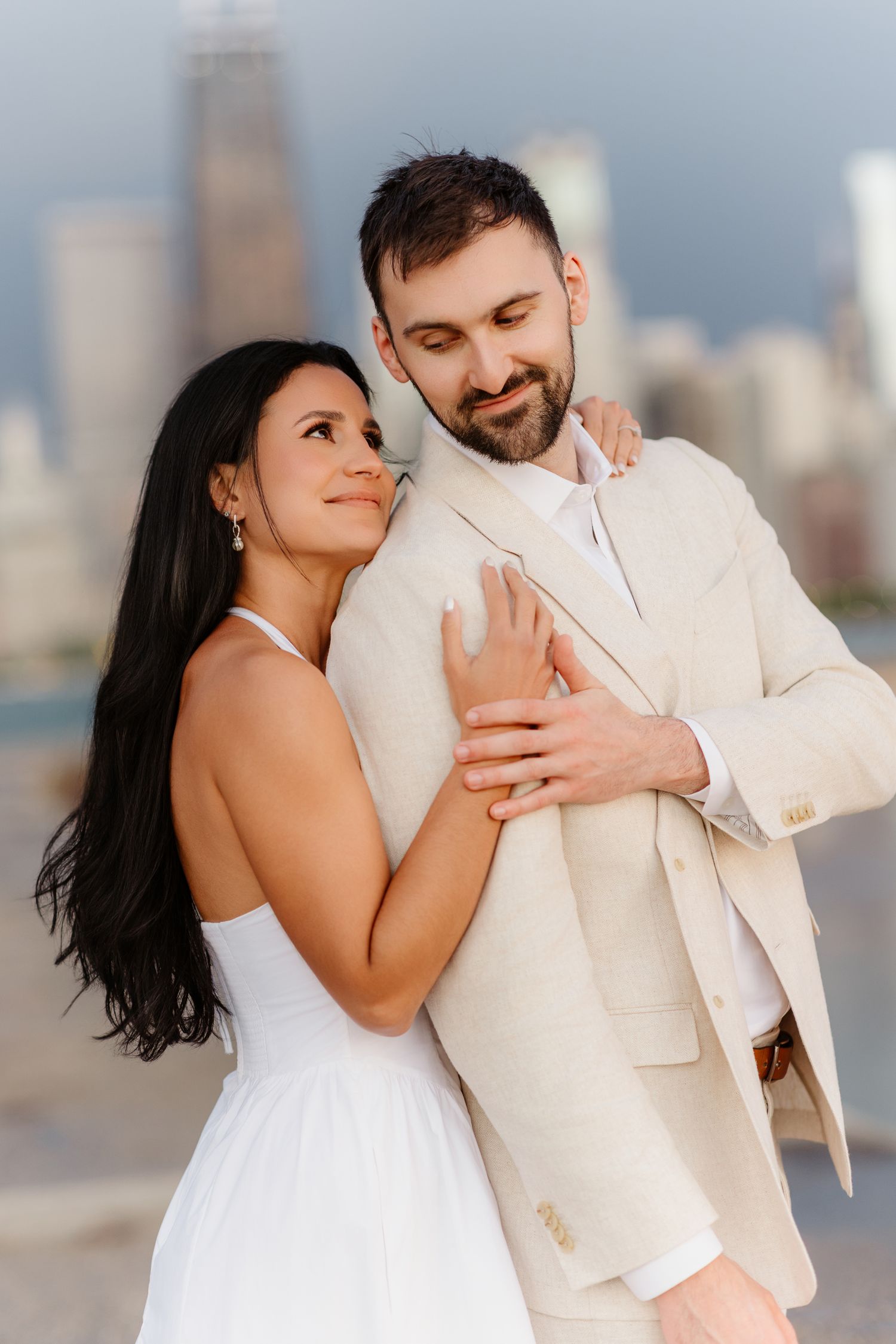 Bride leaning against groom's shoulder while embracing near Chicago waterfront with John Hancock Tower visible.