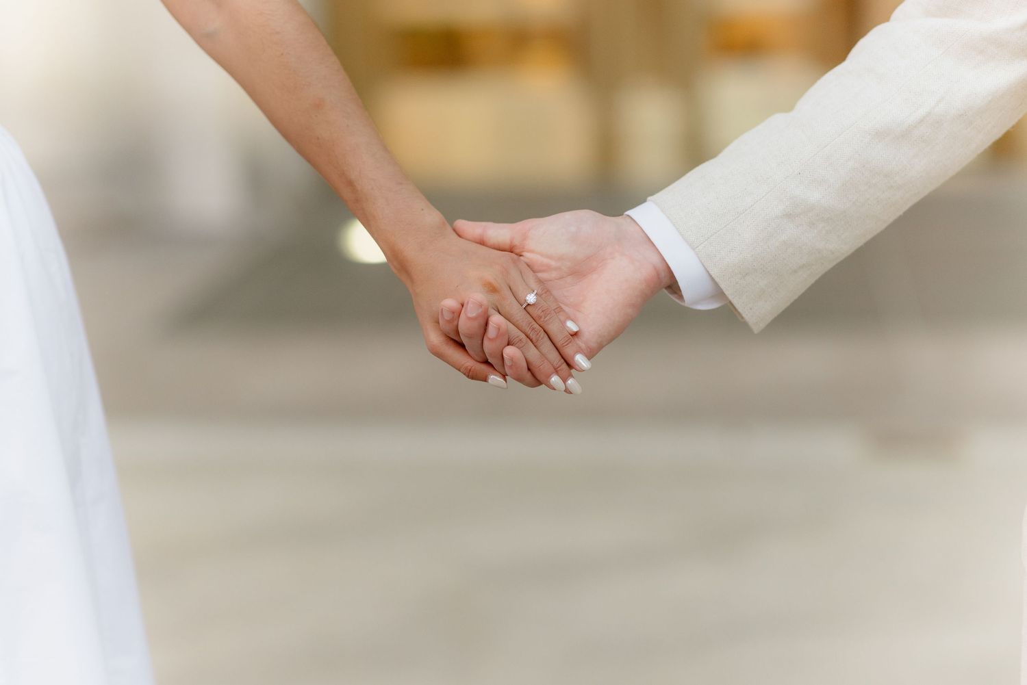 Close-up of couple holding hands showing engagement ring in soft bokeh light.