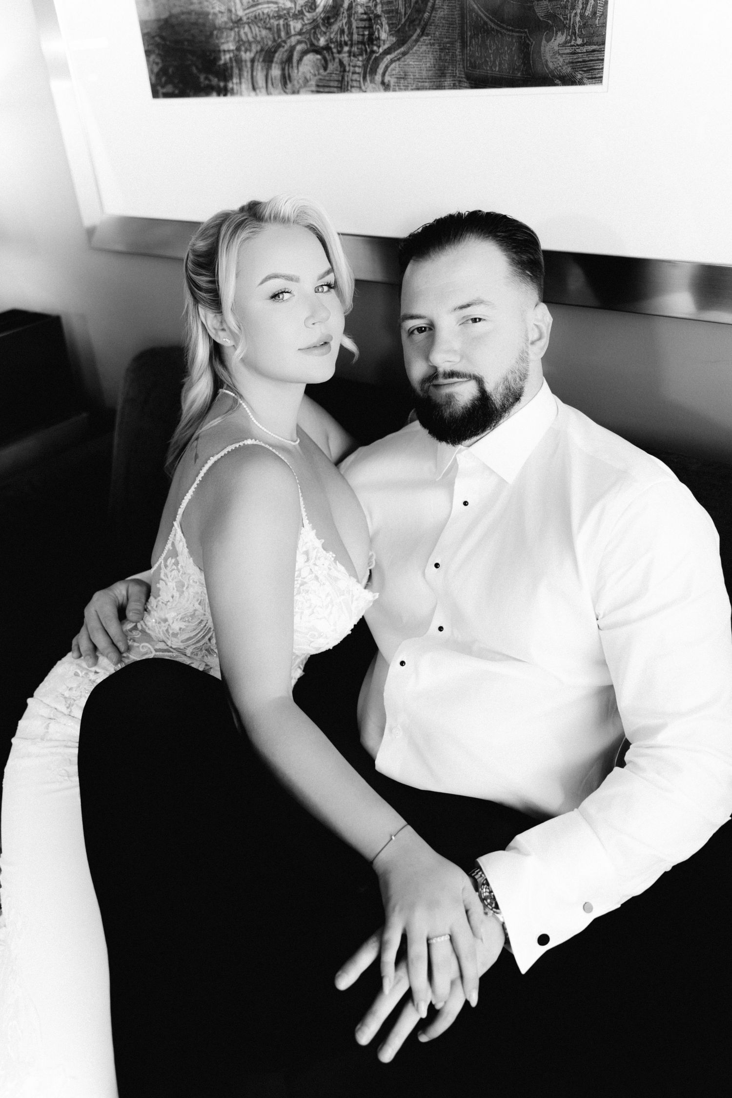 Black and white close-up of blonde bride in lace dress and bearded groom sitting together intimately.