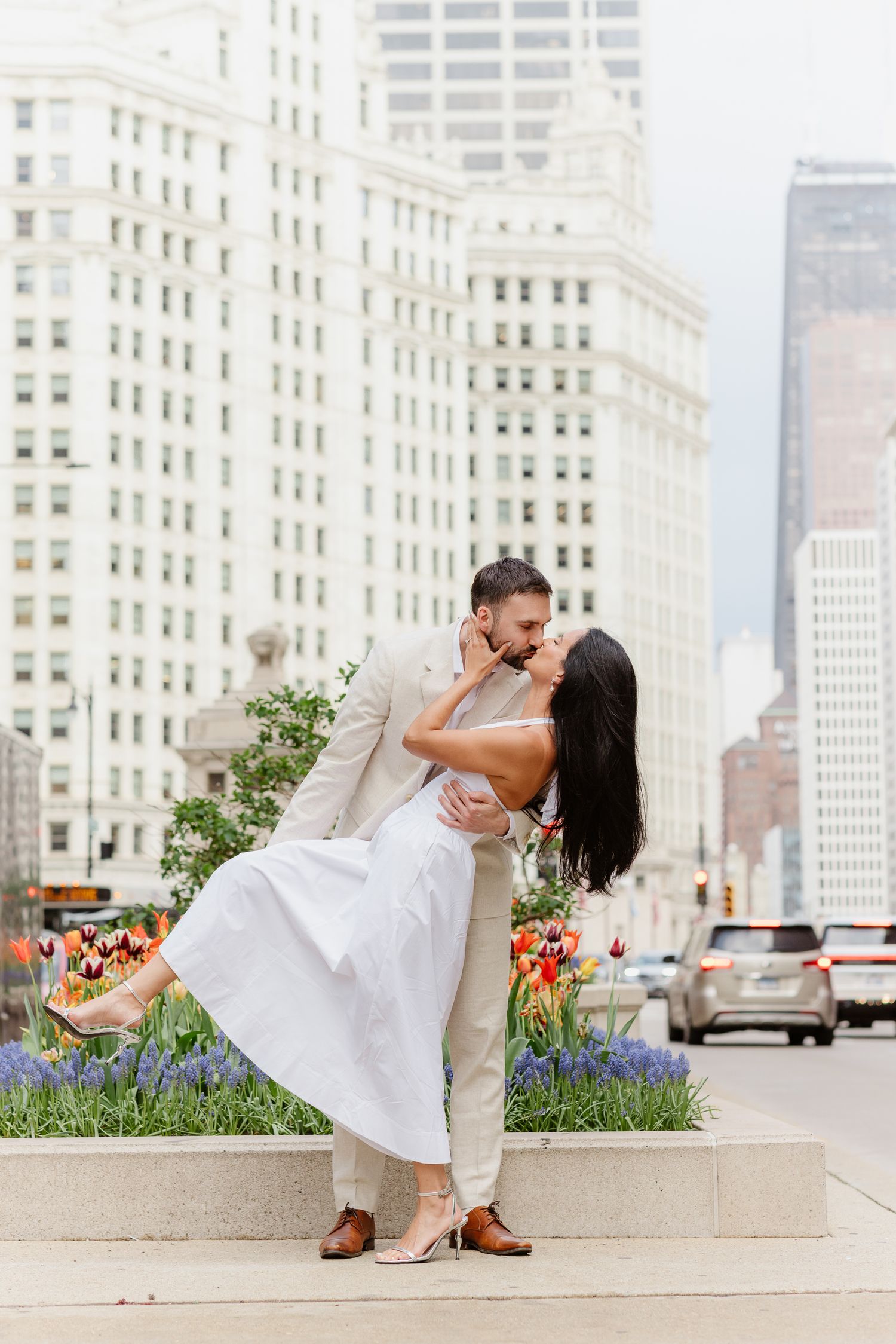 Couple sharing a romantic dip kiss in front of colorful tulips with Chicago city buildings in the background.