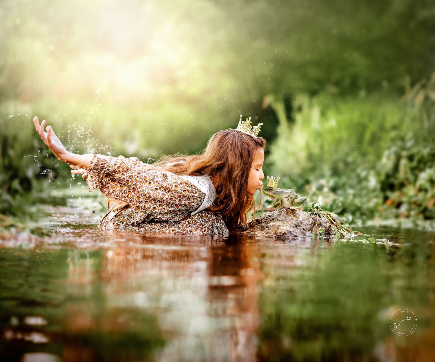 A young girl wearing a floral dress and crown splashes playfully in a sunlit forest stream.
