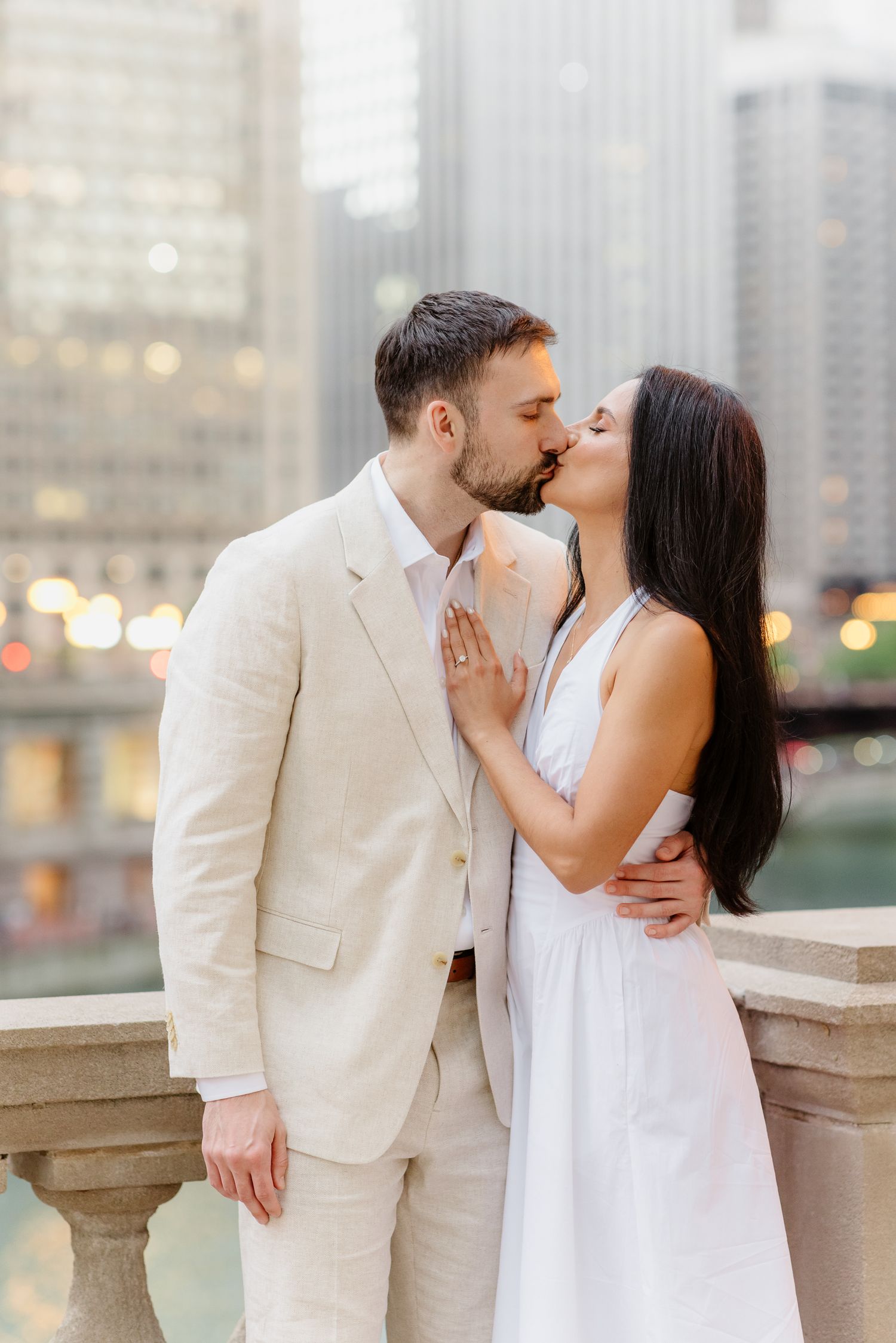 Couple sharing a tender kiss on a stone bridge with Chicago skyscrapers glowing in the background.