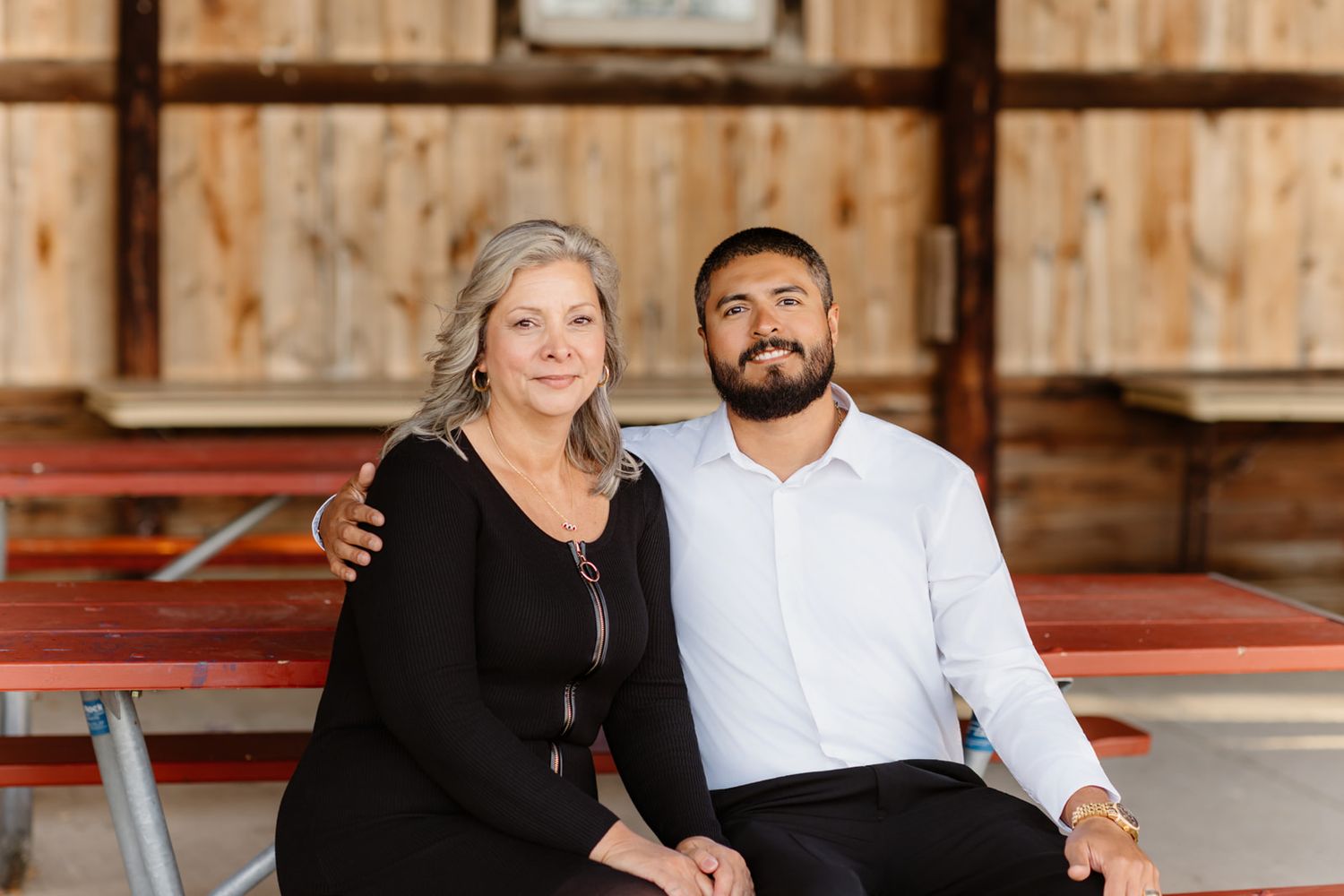 Older woman and young man in white shirt sit together smiling inside a rustic wooden barn venue.