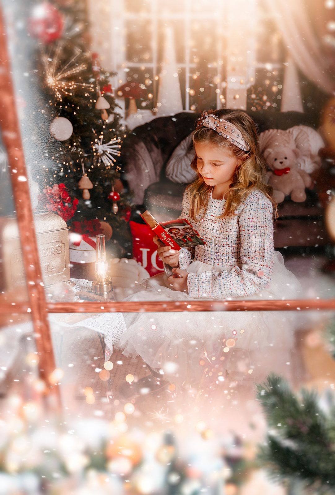 Young girl in tweed dress holds Christmas gift near glowing candle and festive holiday tree.