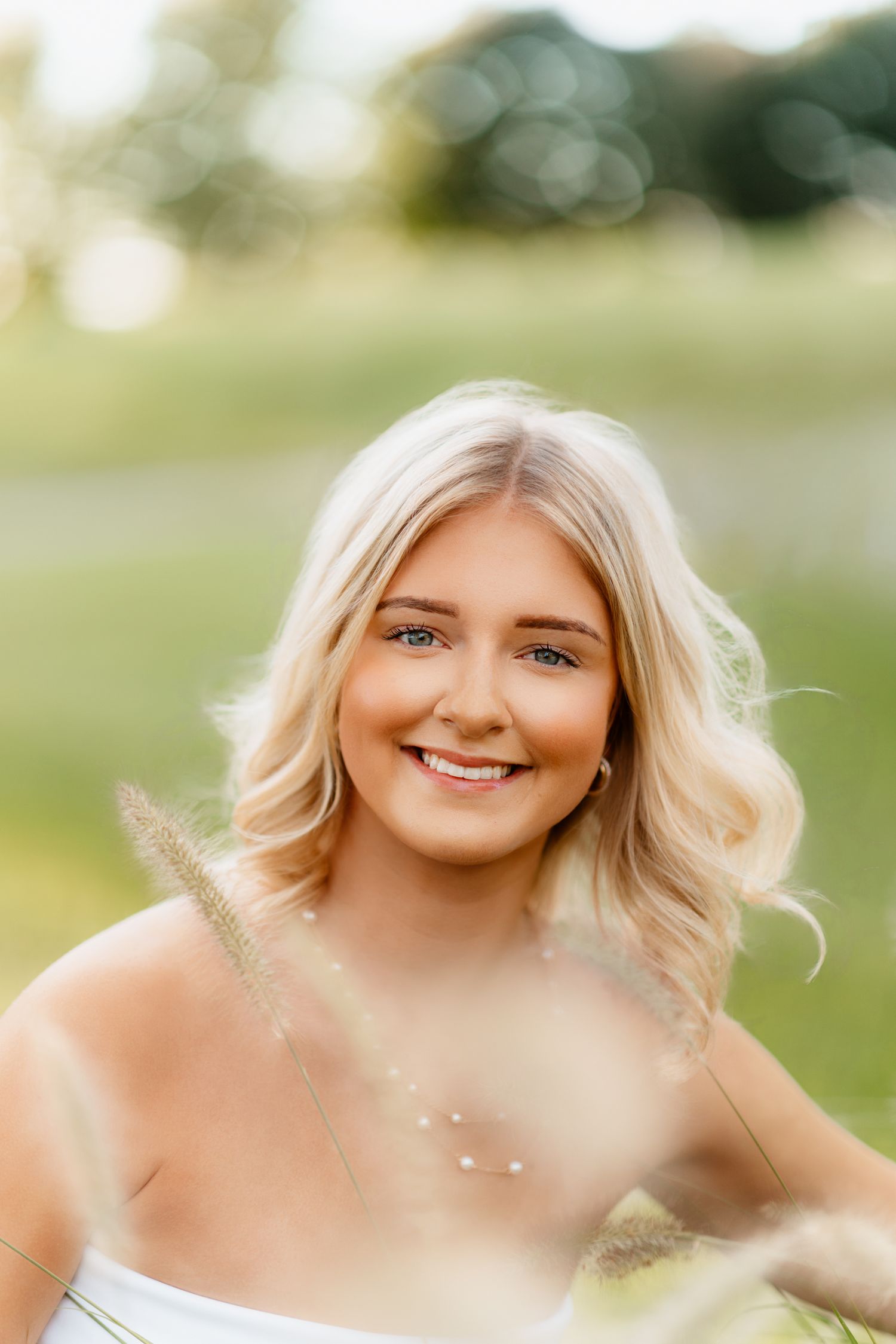 Close-up portrait of smiling blonde woman in white dress in soft outdoor light.