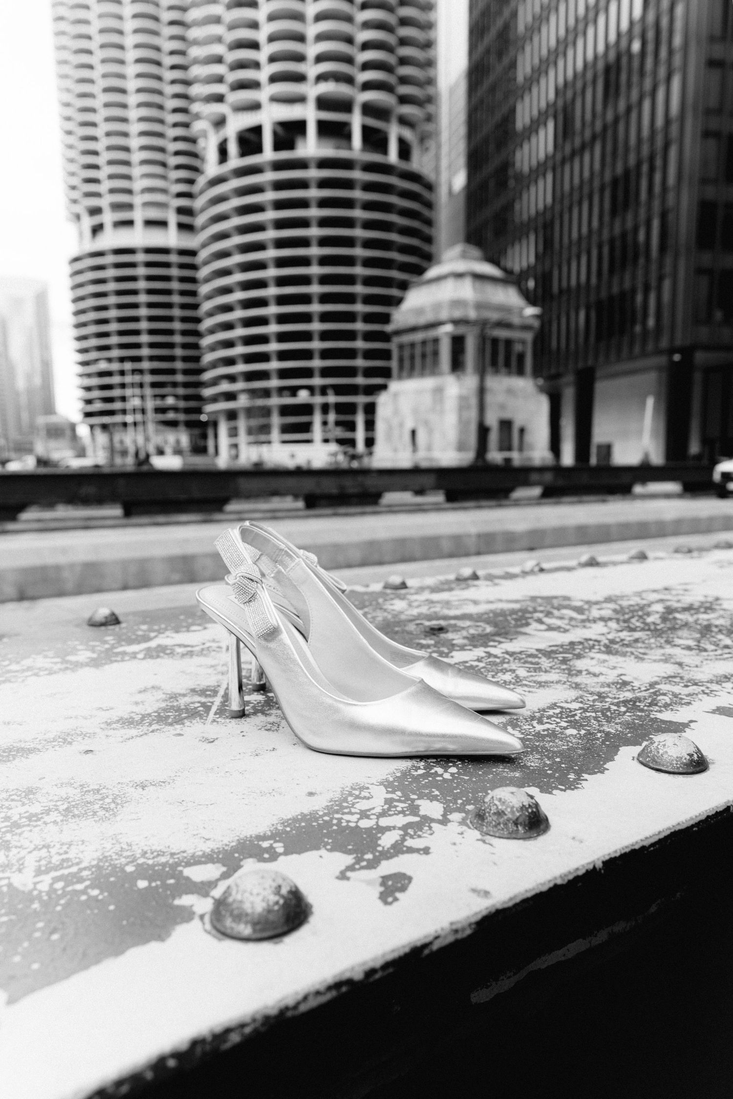 Black and white photo of silver slingback heels on a ledge with Marina City towers in Chicago background.
