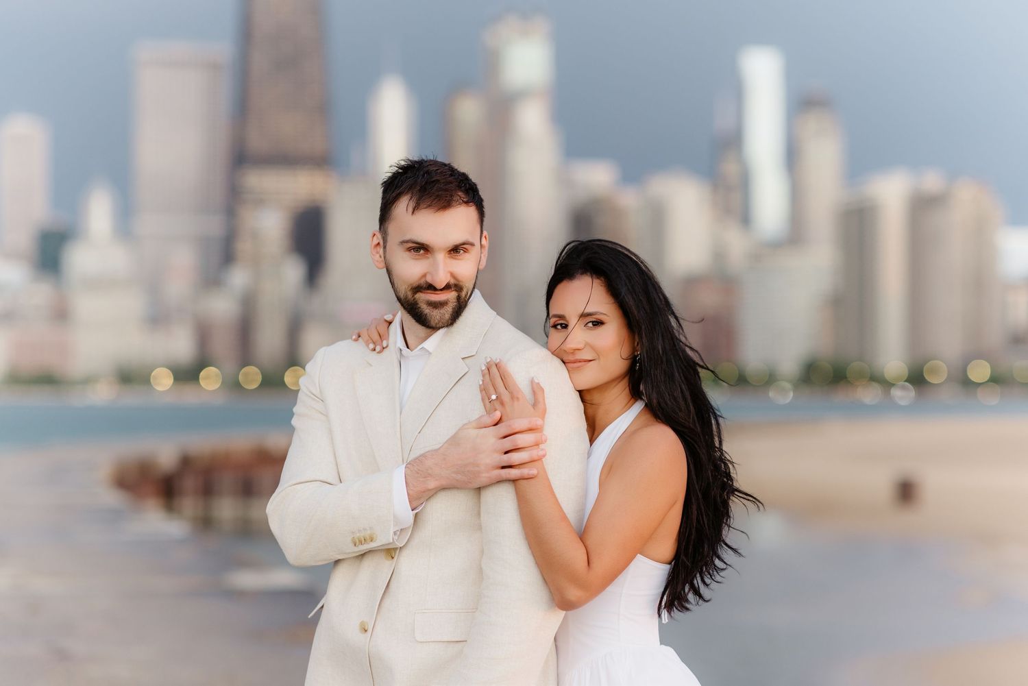 Couple in white wedding attire embracing with Chicago skyline backdrop.
