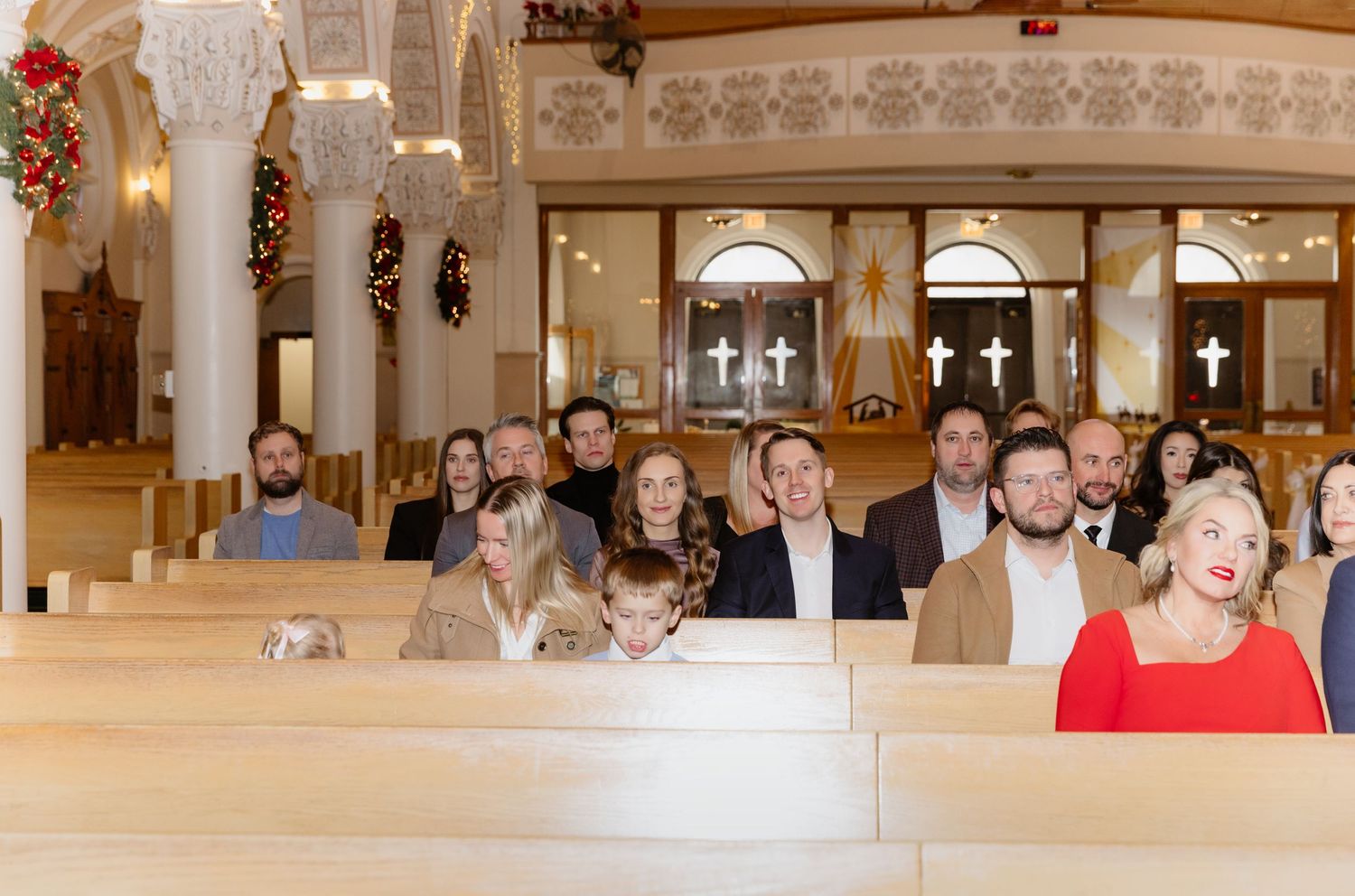 Wedding guests smiling in church pews with ornate white arches and Christmas decorations in the background.