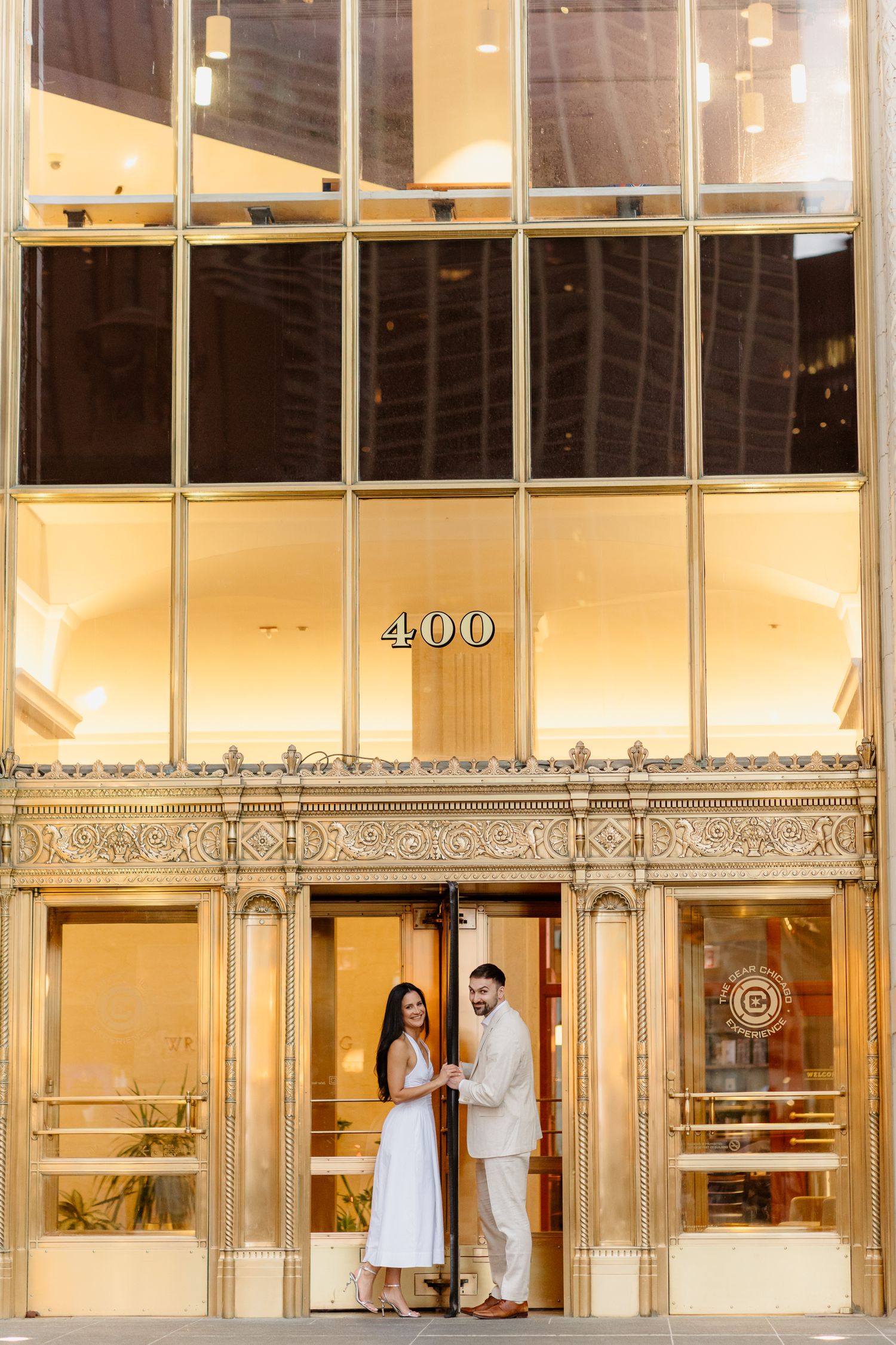 Couple holding hands in front of illuminated 400 address gold Art Deco building entrance.