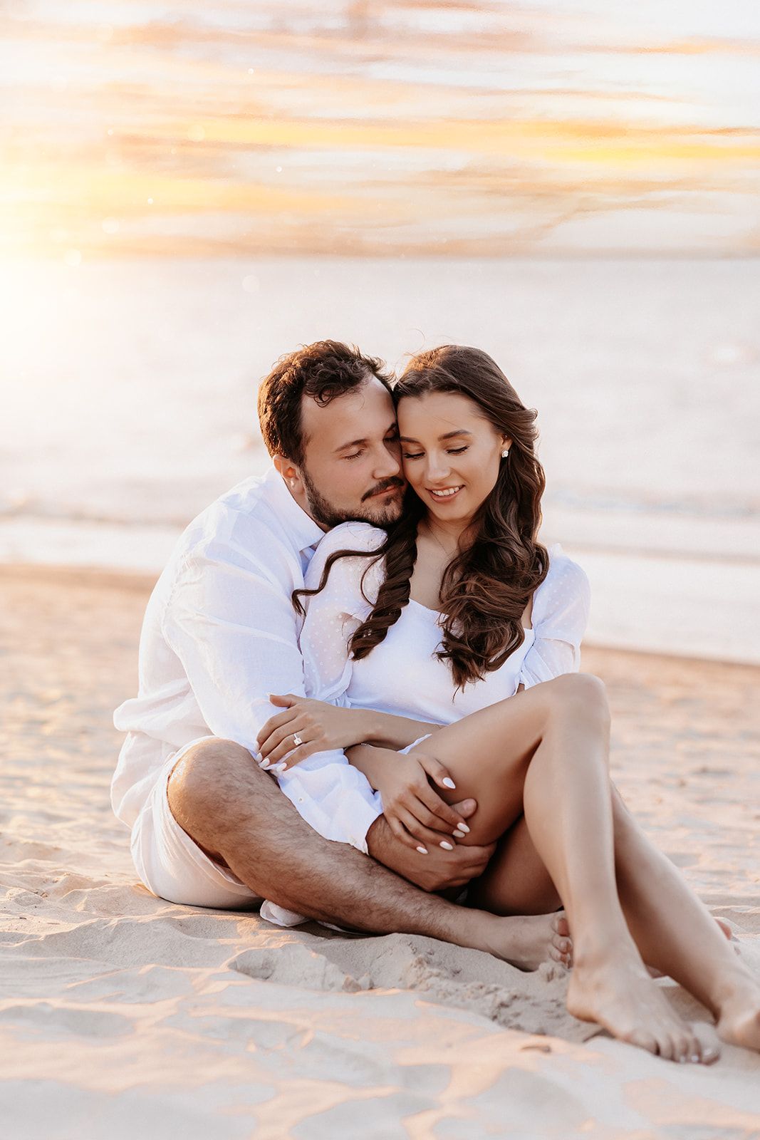 Couple sitting together on the sand, embracing warmly during a golden beach sunset.