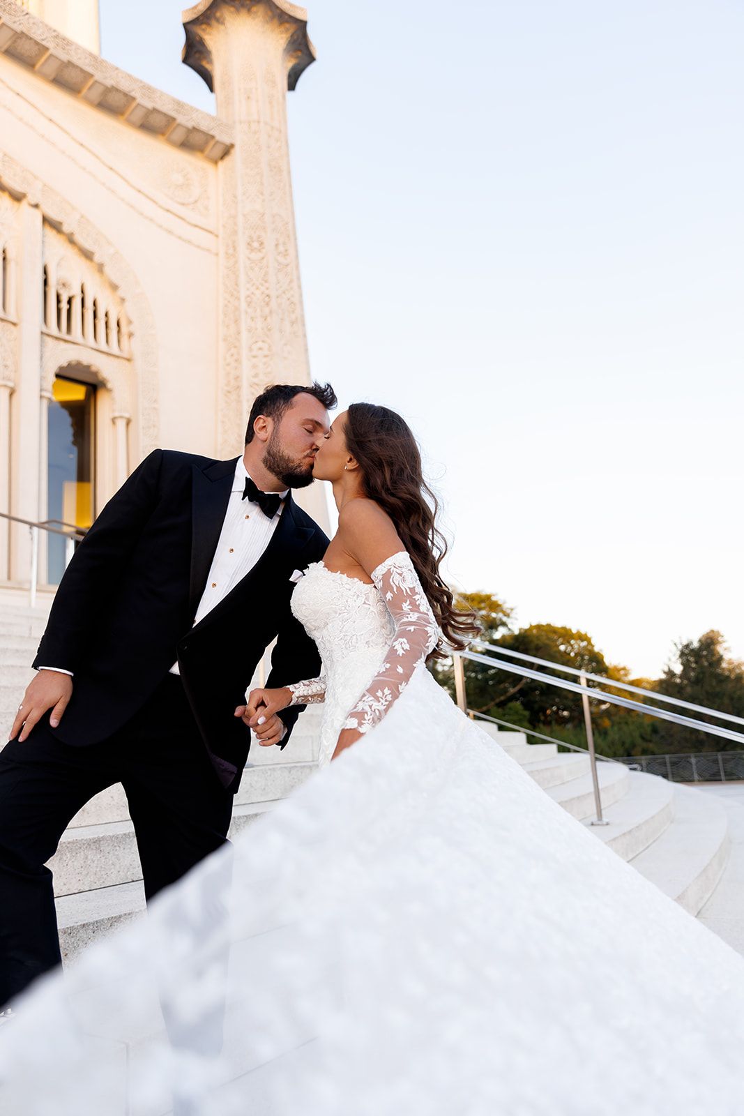 Bride and groom sharing a kiss on steps of elegant venue, bride in lace ball gown.