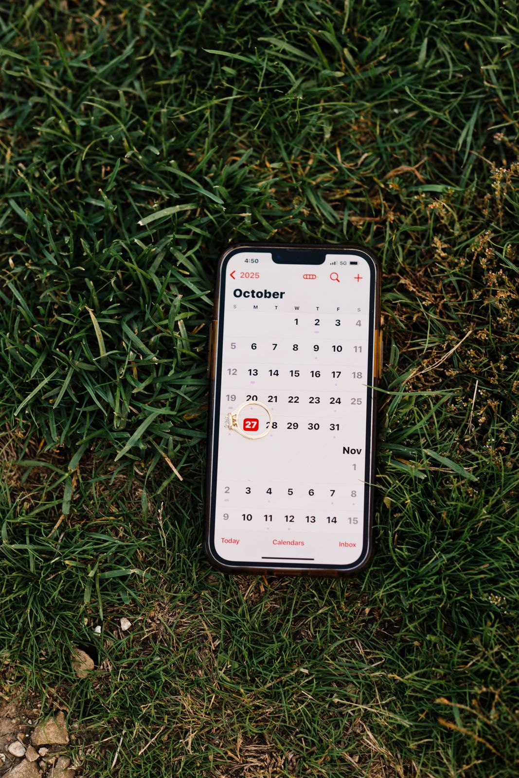 iPhone displaying October calendar app on green grass outdoors.