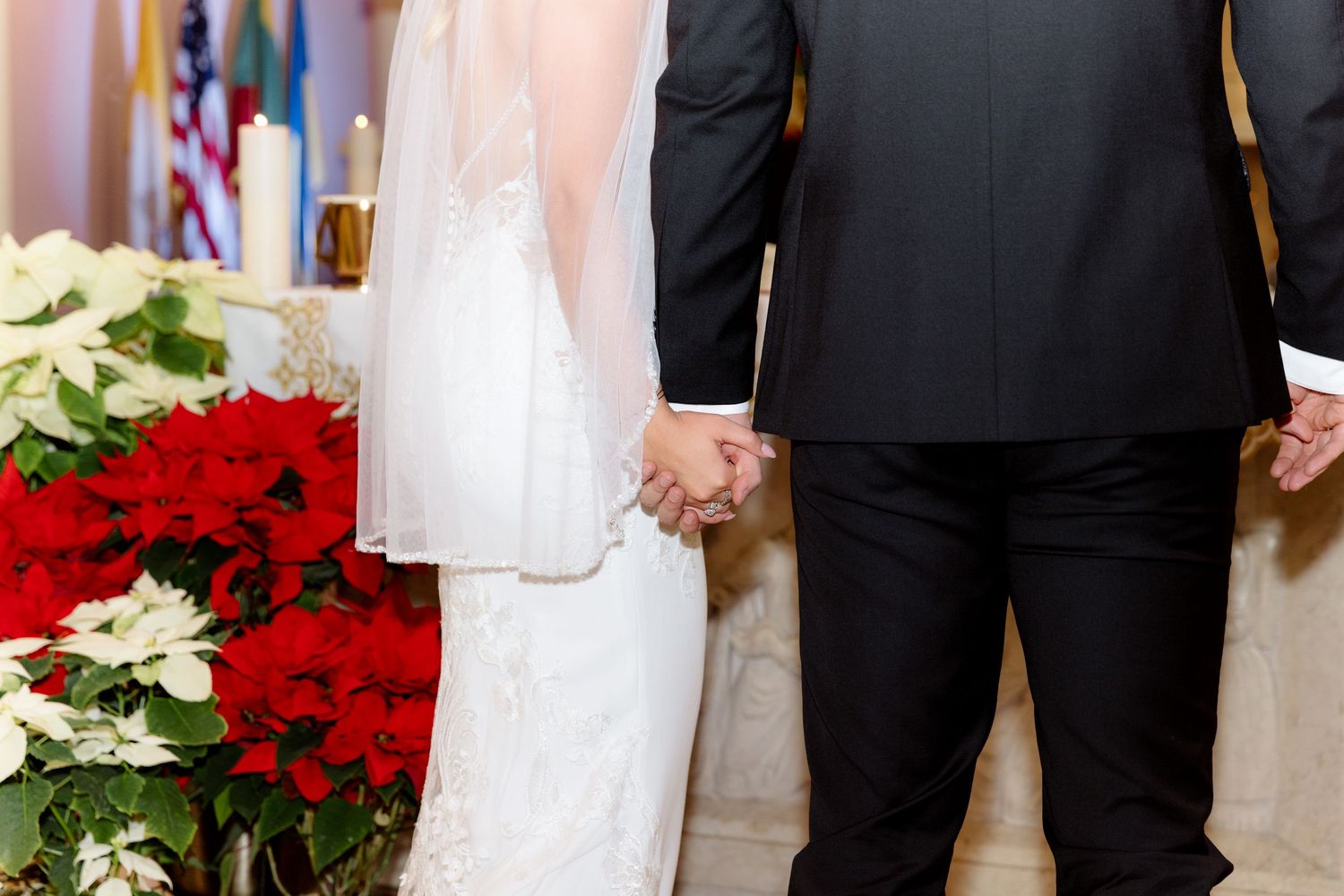 Bride and groom holding hands at altar with red and white poinsettias nearby.