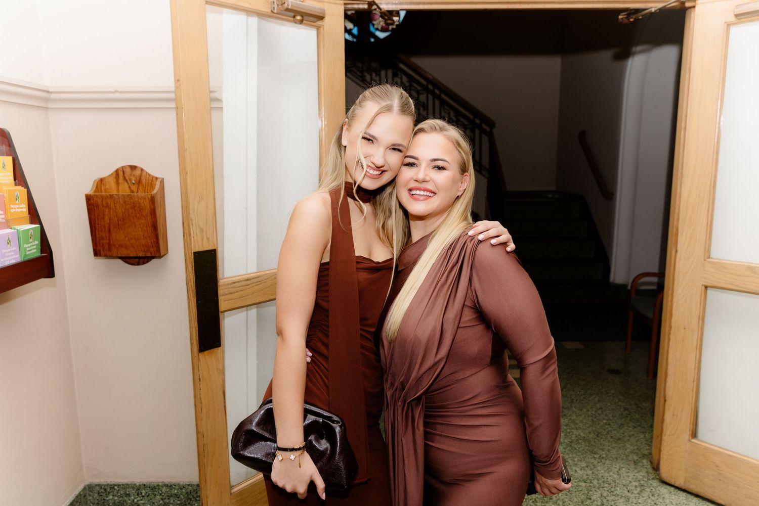 Two young women in elegant brown dresses posing together at formal event.