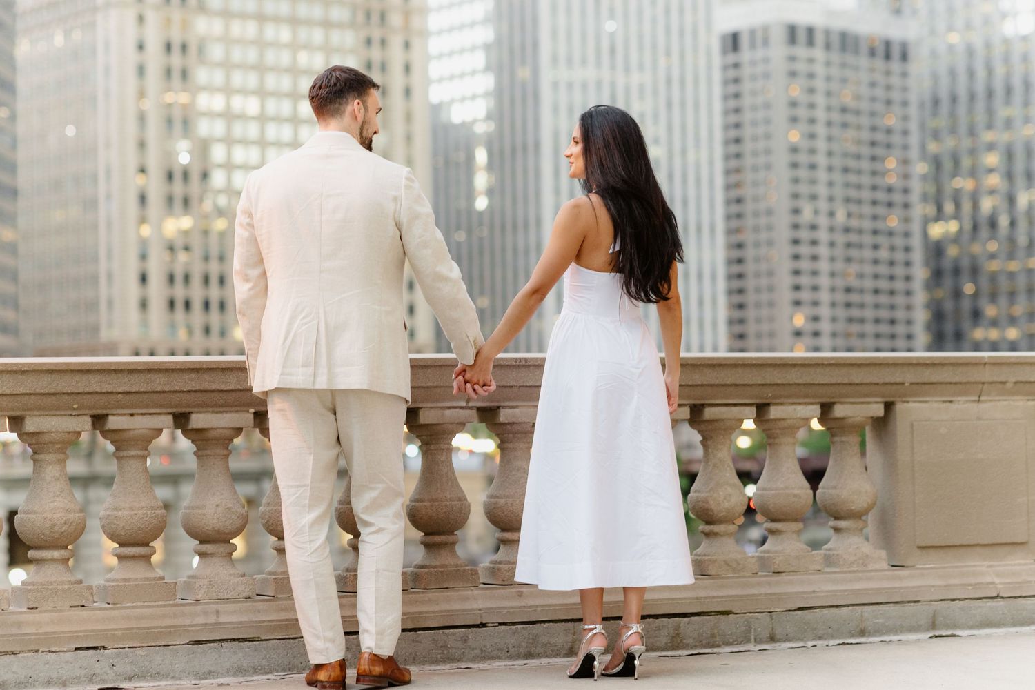 Couple holding hands from behind overlooking Chicago skyline from ornate stone balcony.