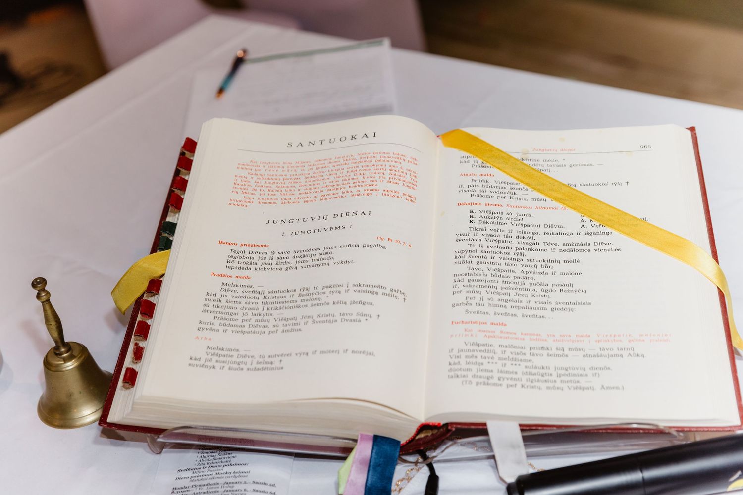 Open red liturgical book with yellow ribbon bookmark on a table during a church ceremony.