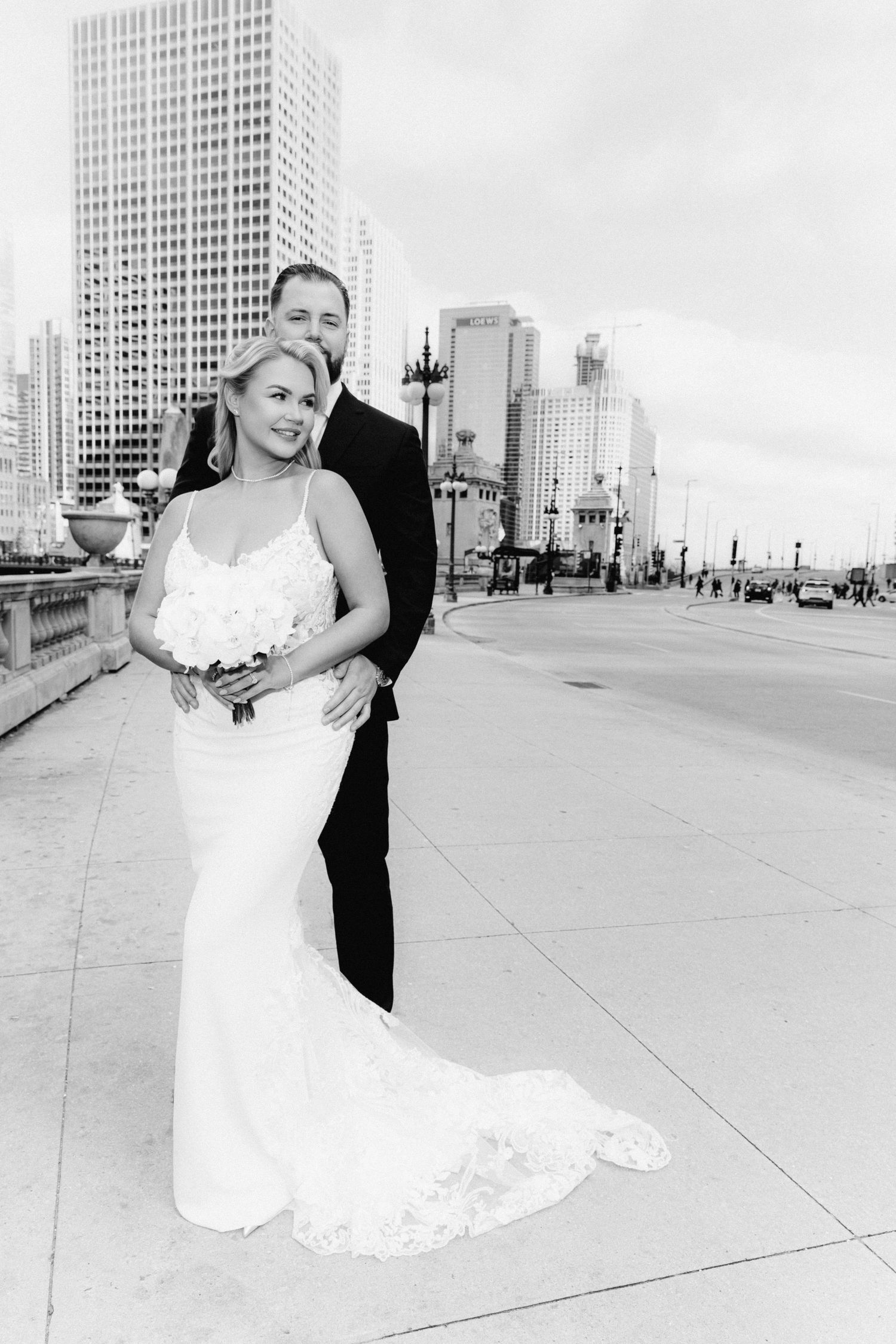 Black and white photo of bride and groom embracing on a Chicago bridge with city skyline behind.