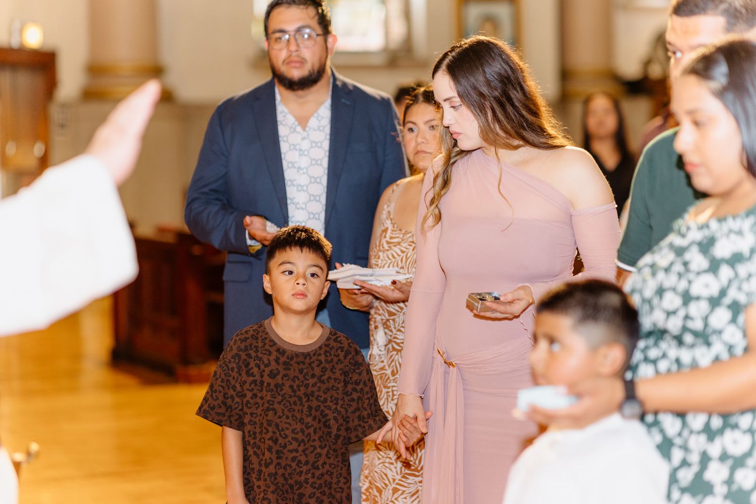 Family gathered in church aisle during a baptism ceremony, dressed in formal attire.