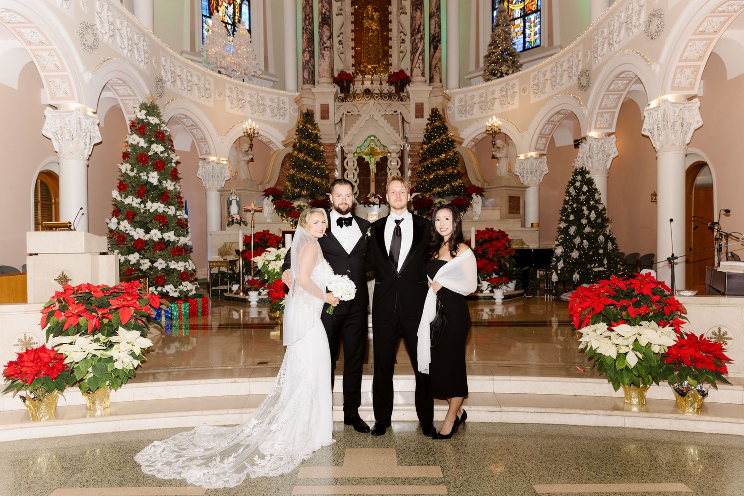 Bride groom and two guests posing in beautifully Christmas-decorated church with poinsettias and trees.