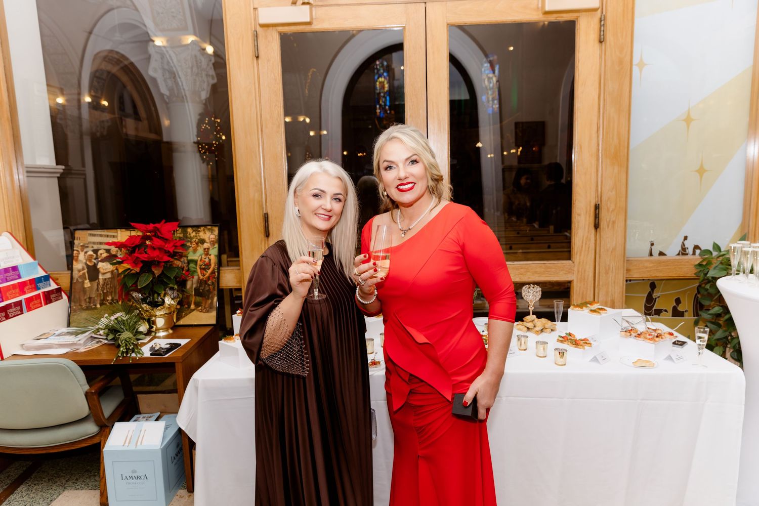 Two smiling women in formal attire raise glasses at a beautifully decorated wedding reception.
