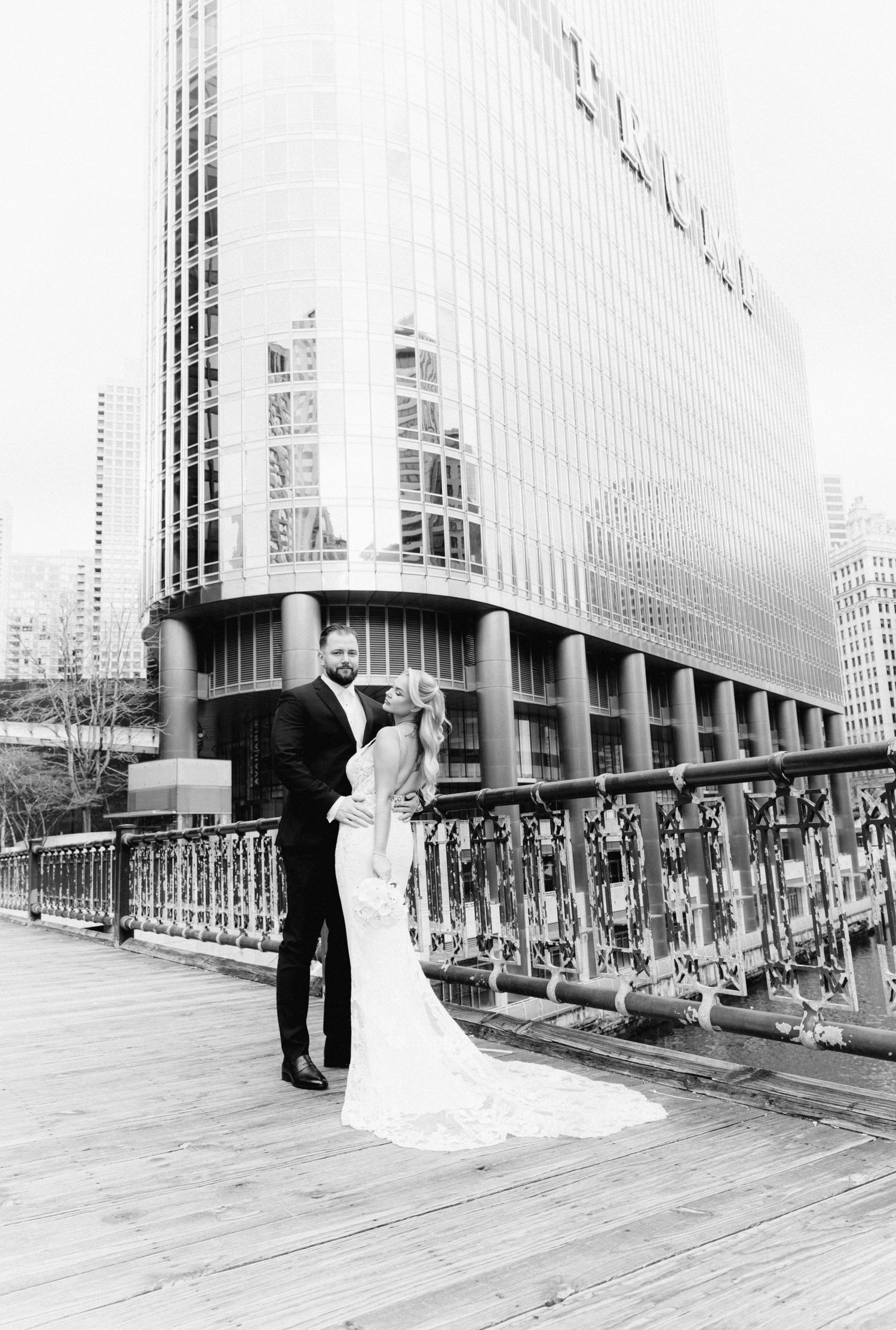 Black and white photo of bride and groom on Chicago Riverwalk with tall buildings.